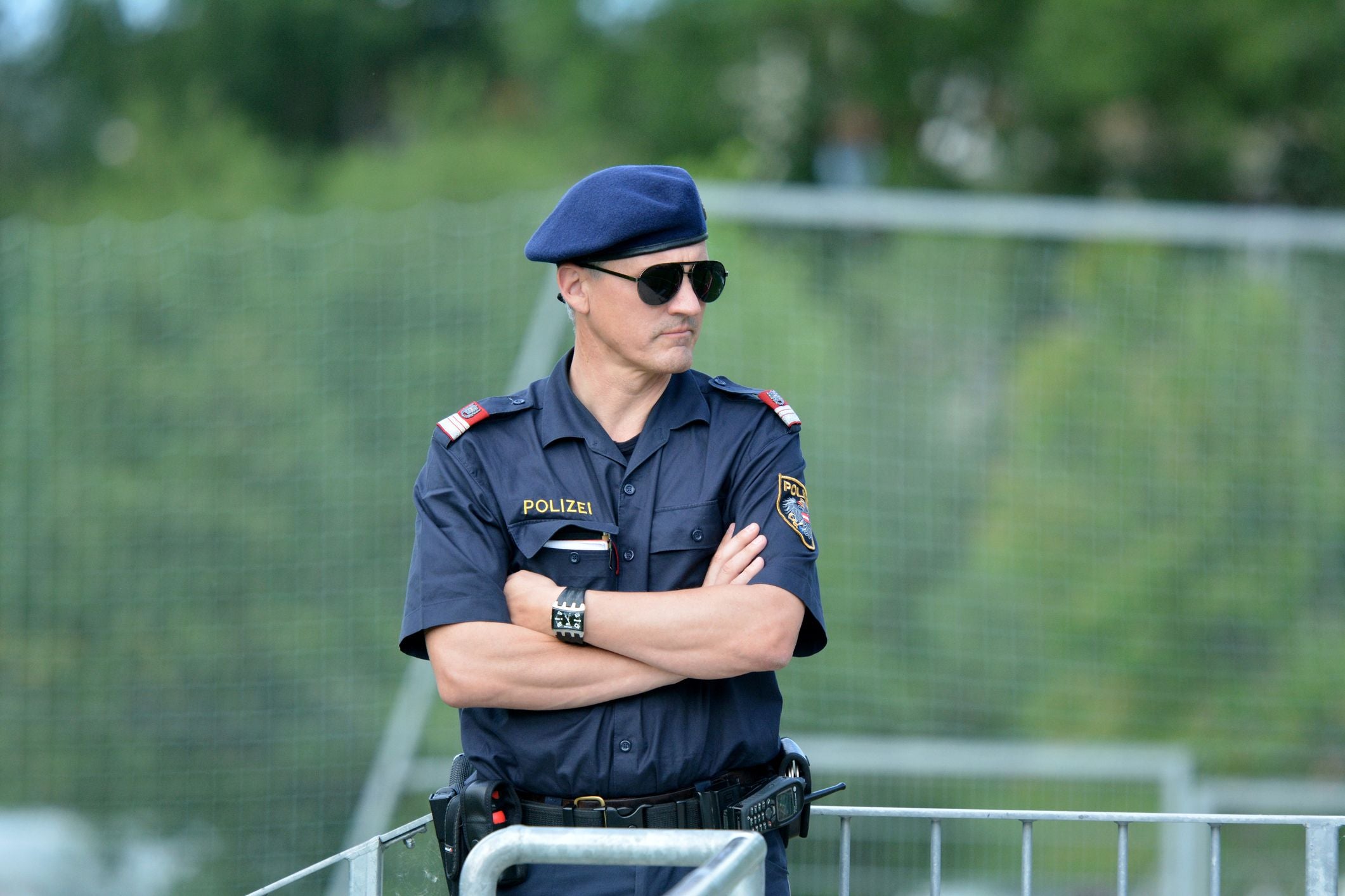 Österreichischer Polizist mit Sonnenbrille und Uniform steht draußen mit verschränkten Armen.
