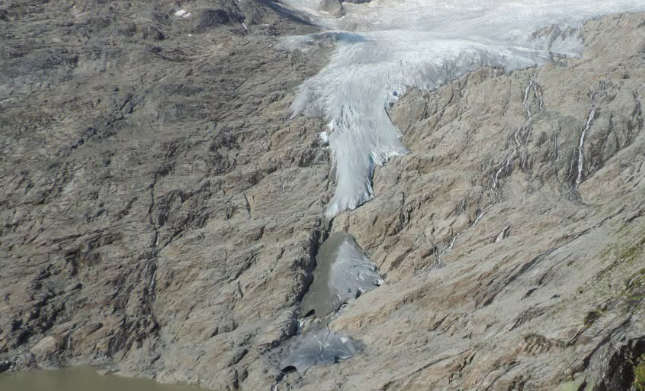 Schmelzender Gletscher fließt ein schmales Tal hinab, umgeben von steinigem Gelände.