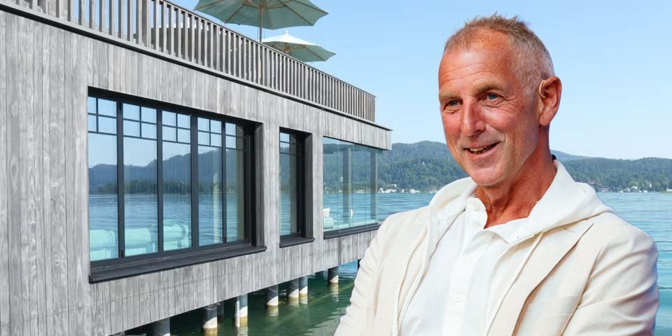 Ein älterer Mann in heller Kleidung steht vor einem modernen Haus am Wasser.