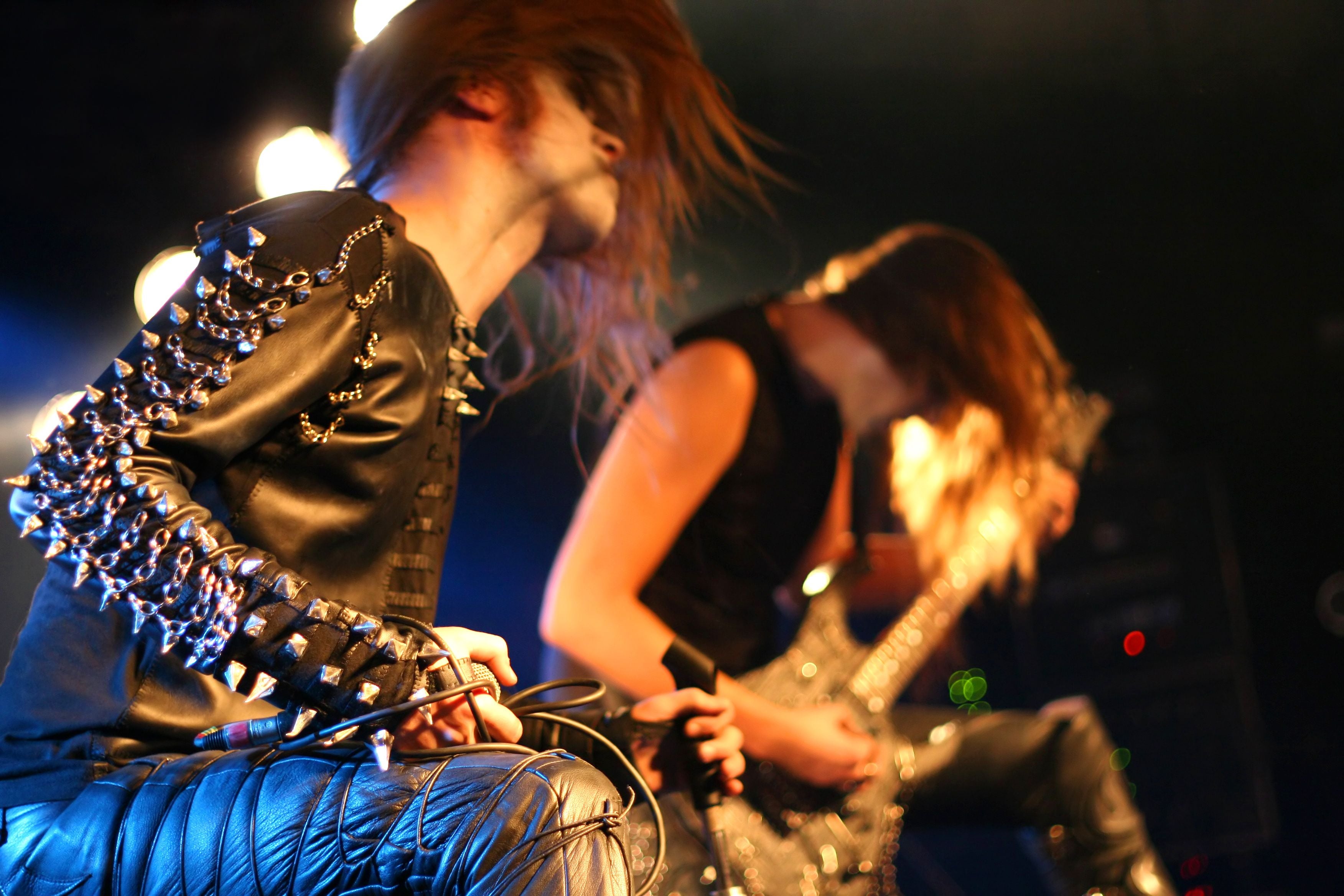 Zwei Mitglieder einer Black-Metal-Band headbangen auf einer Bühne mit starker Bühnenbeleuchtung.