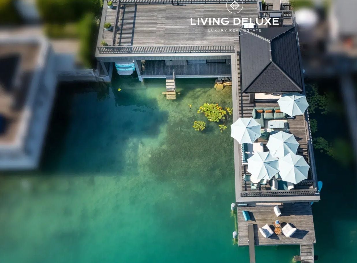 Luftaufnahme einer luxuriösen Terrasse mit weißen Sonnenschirmen direkt am türkisfarbenen Wasser.