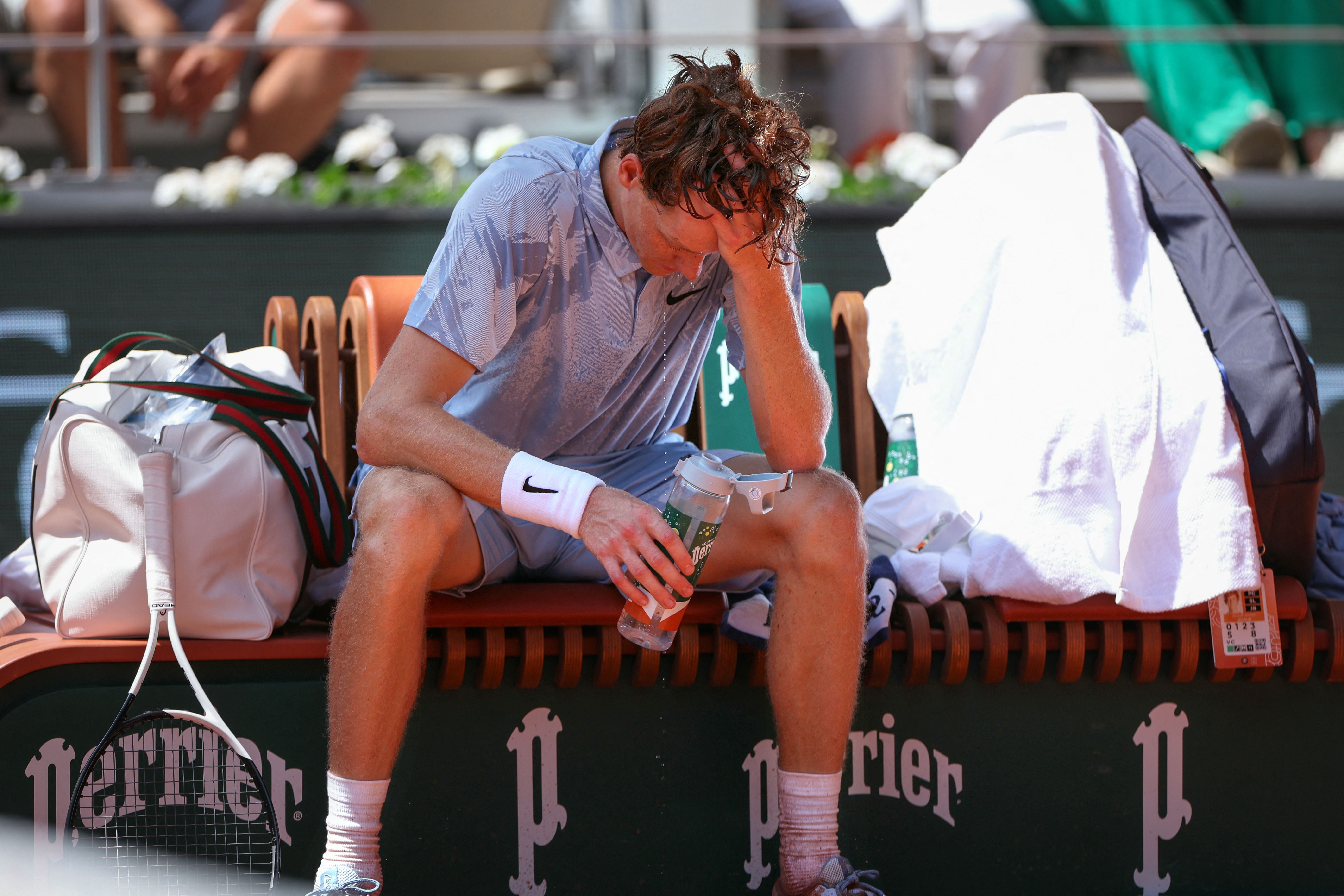Ein erschöpfte Tennisspieler kühlt sich während einer Spielpause mit Wasser auf der Bank ab.