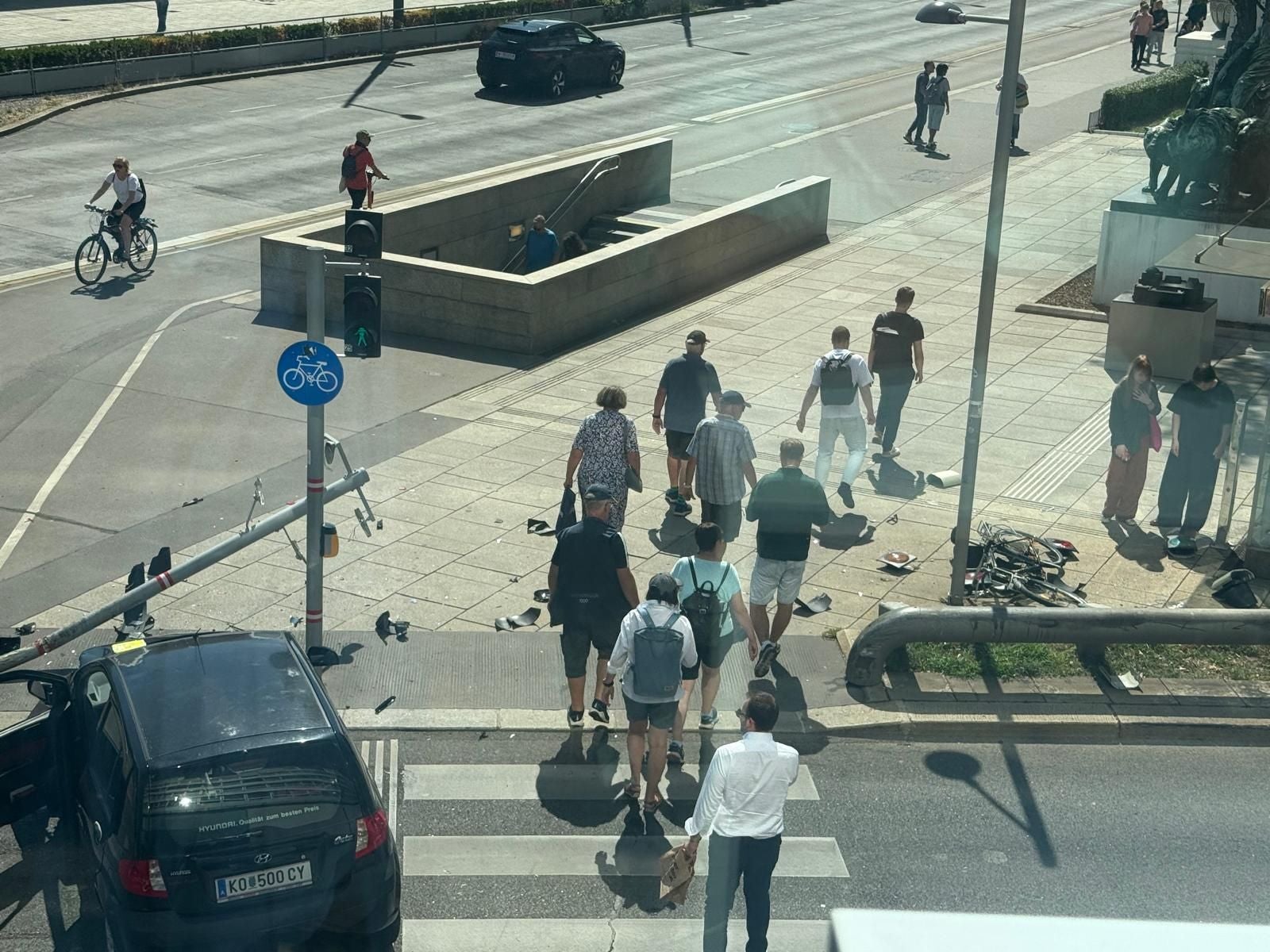 Mehrere Menschen überqueren eine Straße an einem beschädigten Zebrastreifen mit Trümmern und Auto.