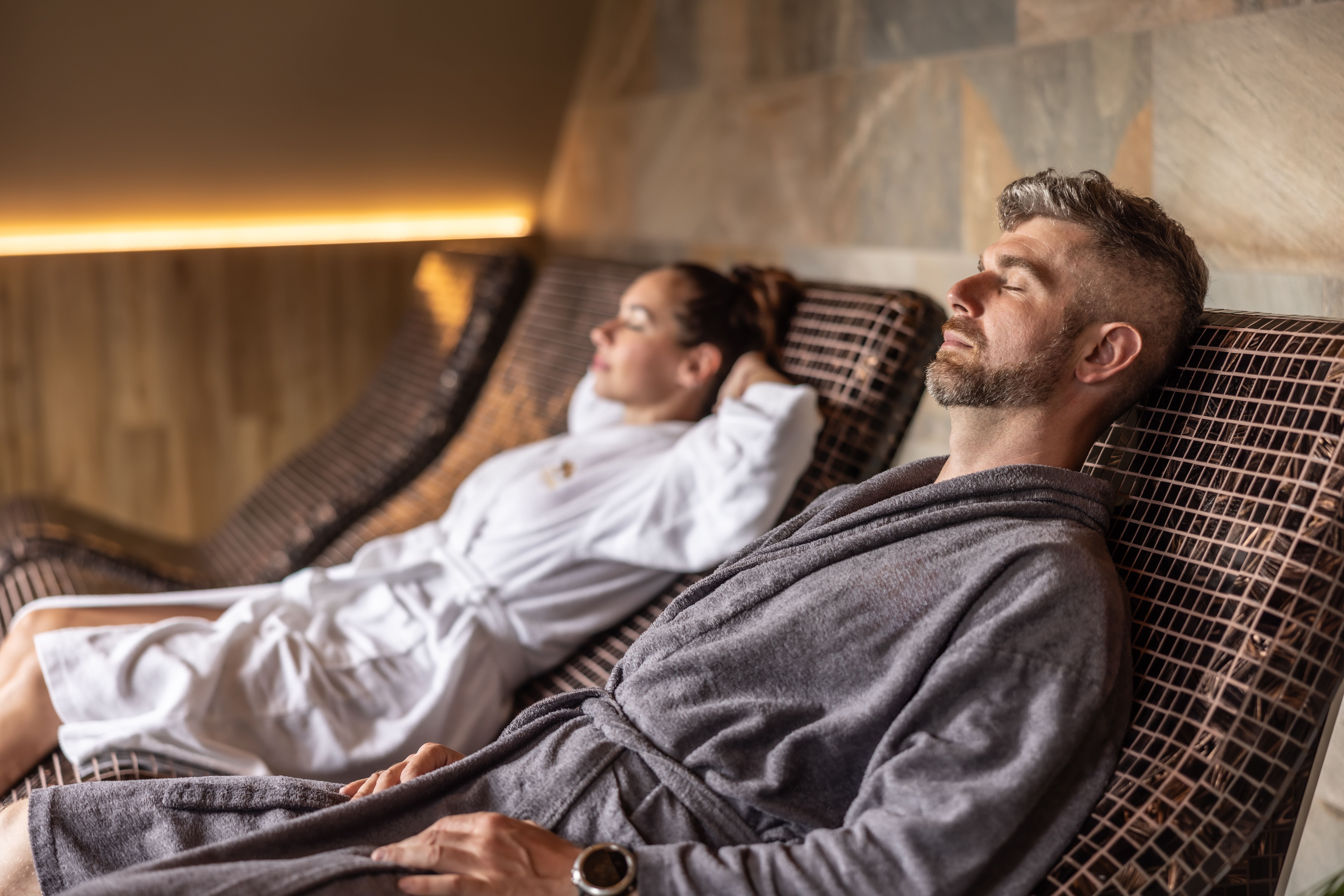 Junges Paar entspannt auf beheizten Liegen im Spa, beide im Bademantel.