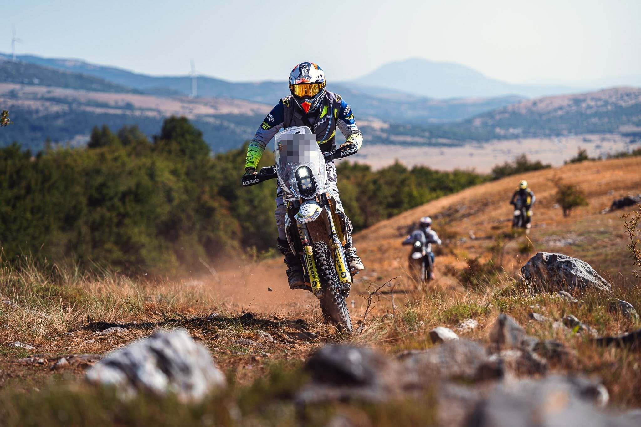 Motorradfahrer fahren bei der Dinaric Rallye über einen steinigen Feldweg in hügeliger Landschaft.