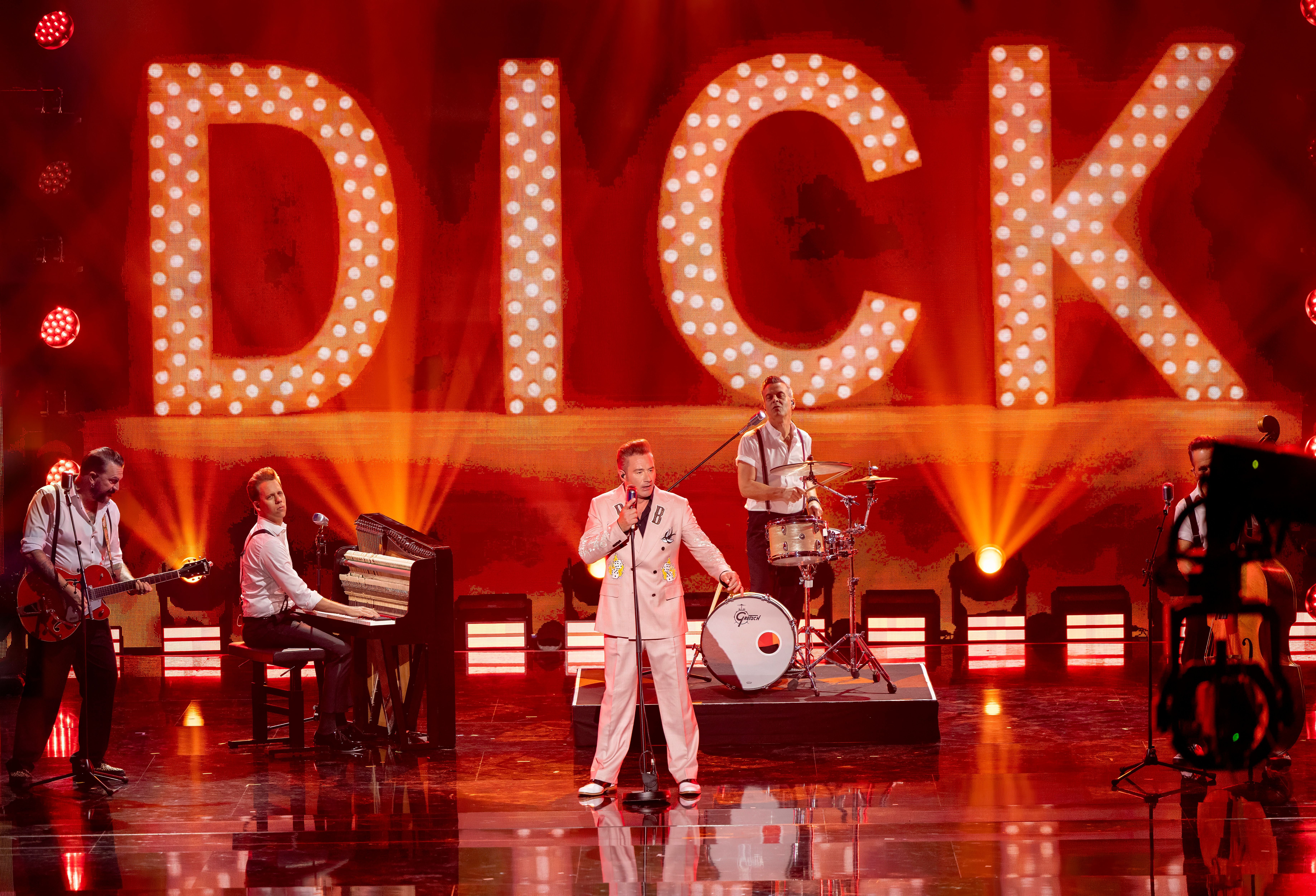 Bandauftritt auf einer Bühne mit großem, leuchtendem "DICK"-Schriftzug im Hintergrund.