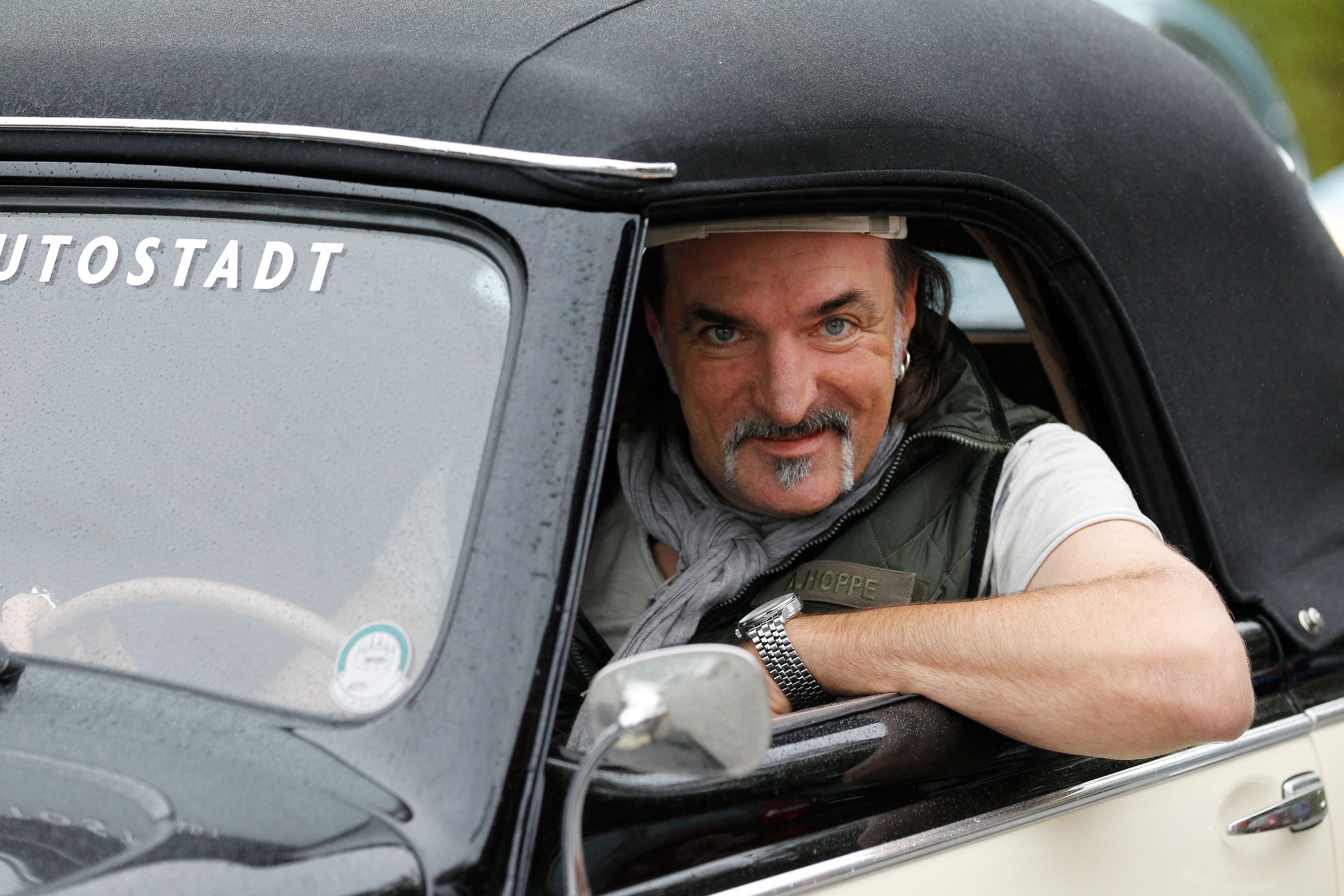 Mann mit Bart lächelt aus dem Fenster eines Oldtimers während einer Oldtimer-Rallye.