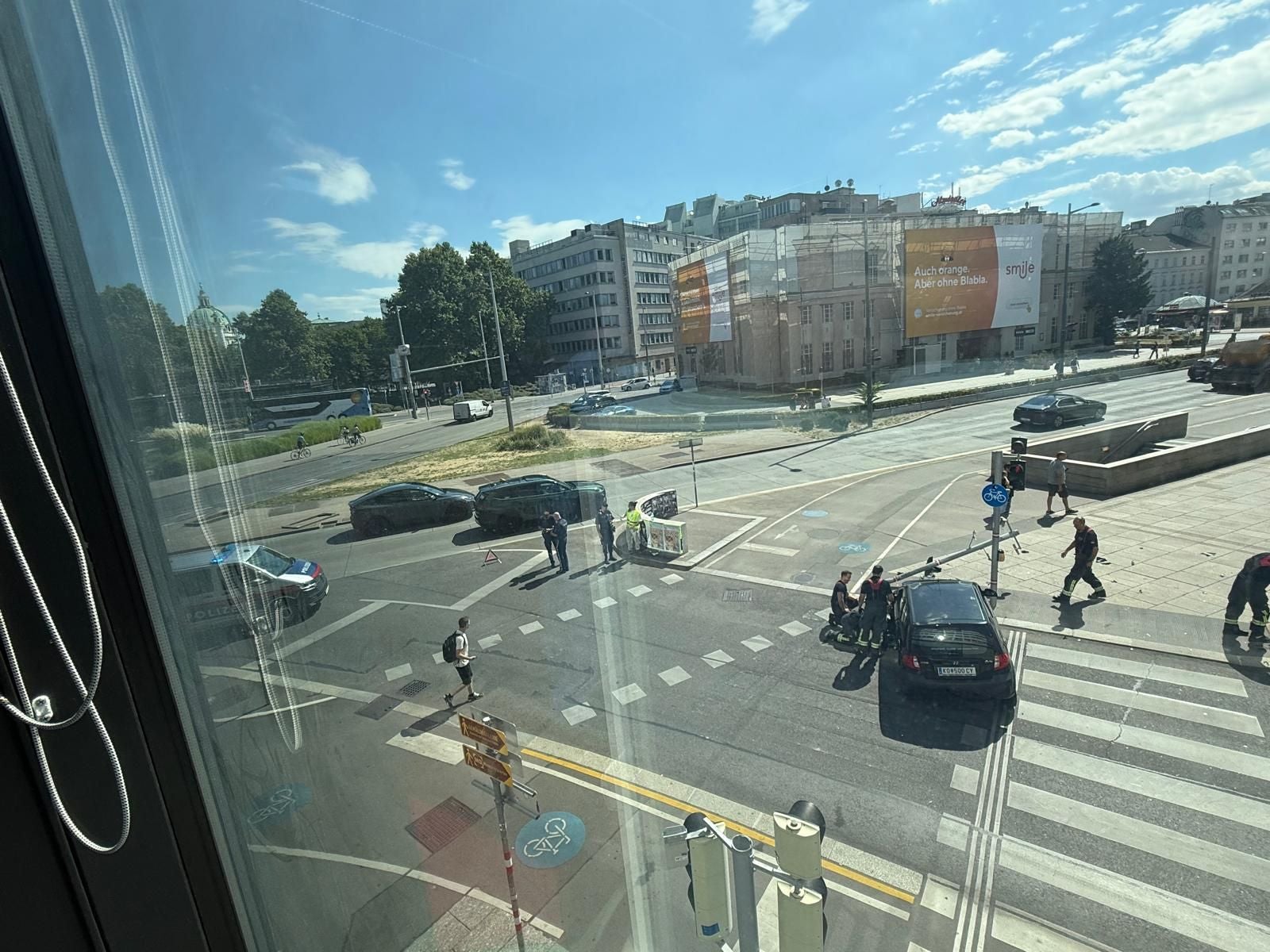 Blick auf eine Straßenkreuzung mit Polizei, Fußgängern, Autos und sonnigem Wetter.