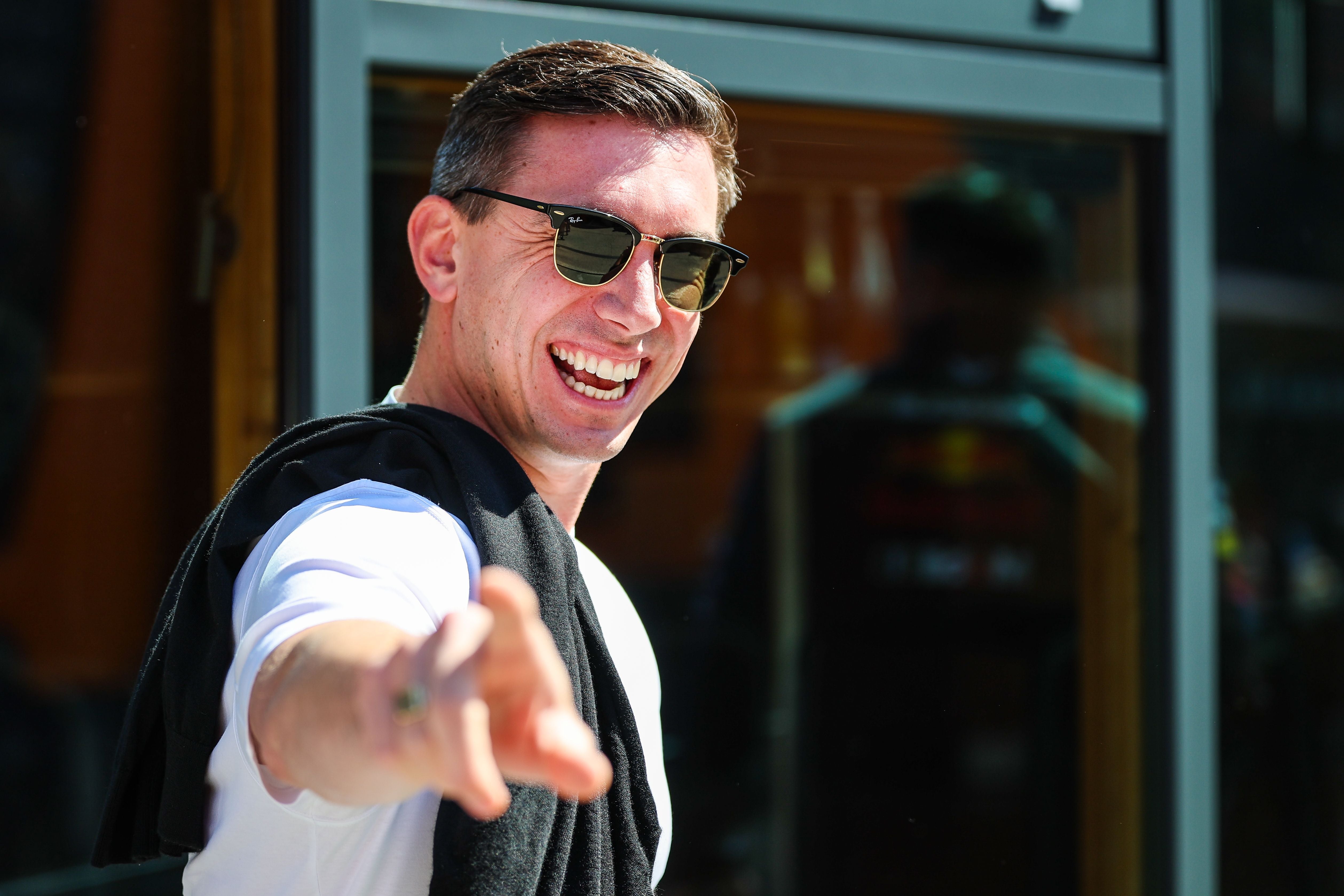 Ein lachender Mann mit Sonnenbrille zeigt in die Kamera, im Hintergrund Glasfassade.