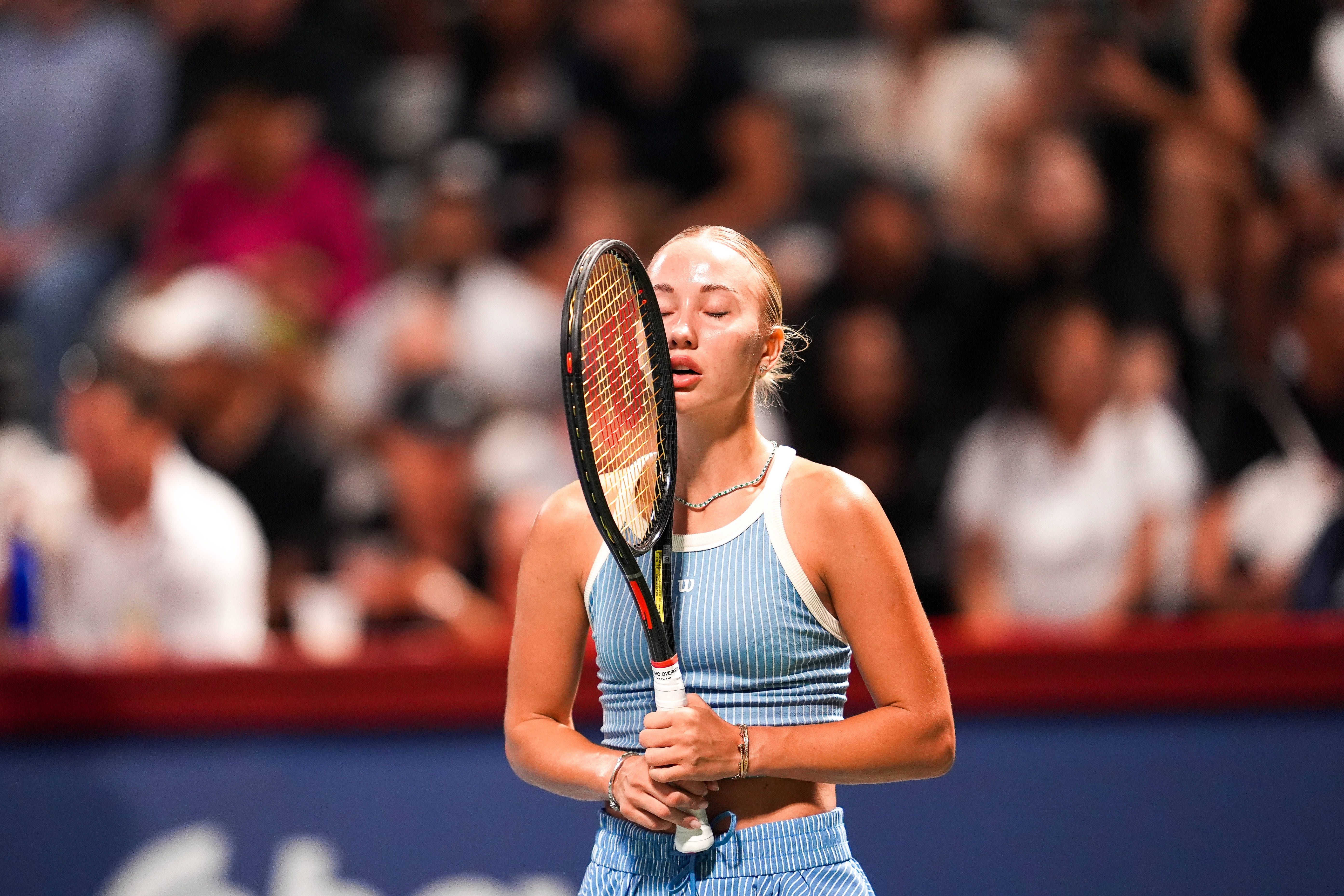 Tennisspielerin hält den Schläger vor ihr Gesicht und wirkt frustriert während eines Spiels.