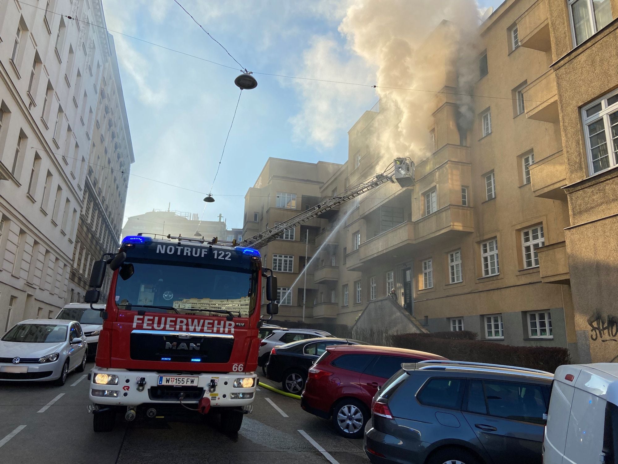 Feuerwehr bekämpft einen Wohnhausbrand mit einer Drehleiter, Rauch steigt aus dem Gebäude auf.