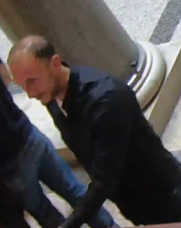 Ein Mann in dunkler Kleidung steht in einem Gebäude mit Marmorsäule.