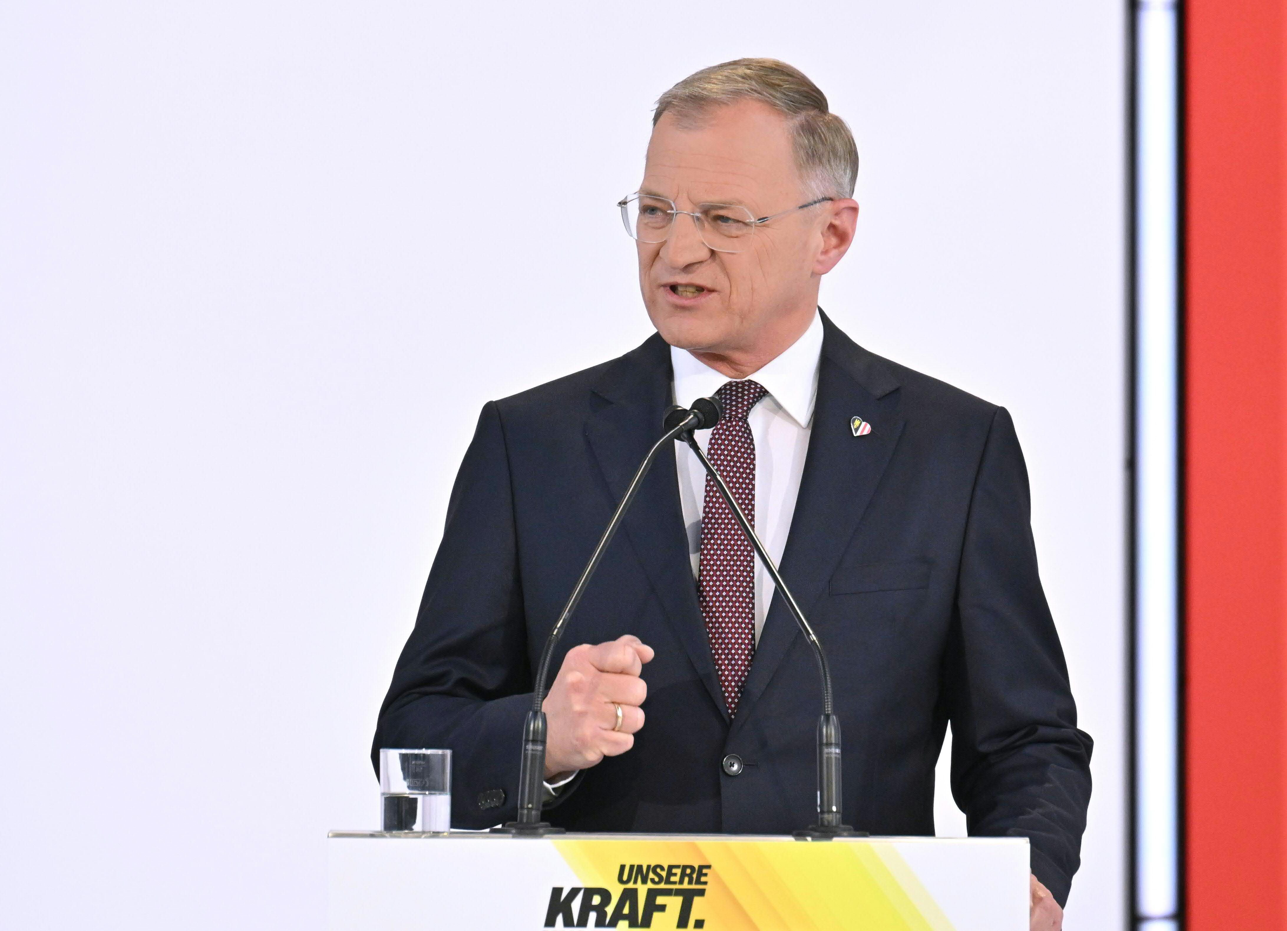 Ein Mann im Anzug spricht am Rednerpult mit Mikrofonen und einem Glas Wasser.