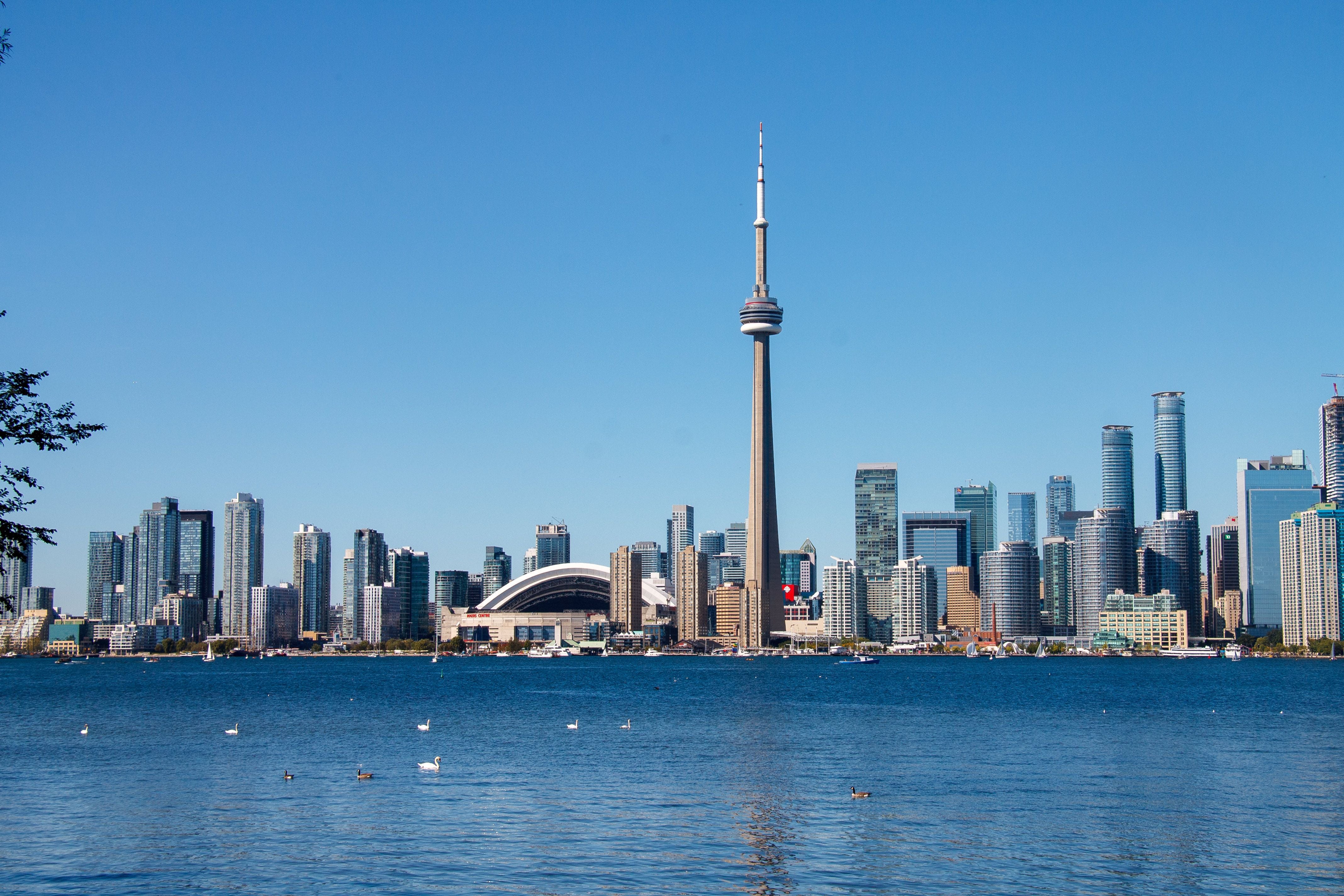 Blick auf die Skyline von Toronto mit CN Tower und Rogers Centre am Ontariosee bei klarem Himmel.