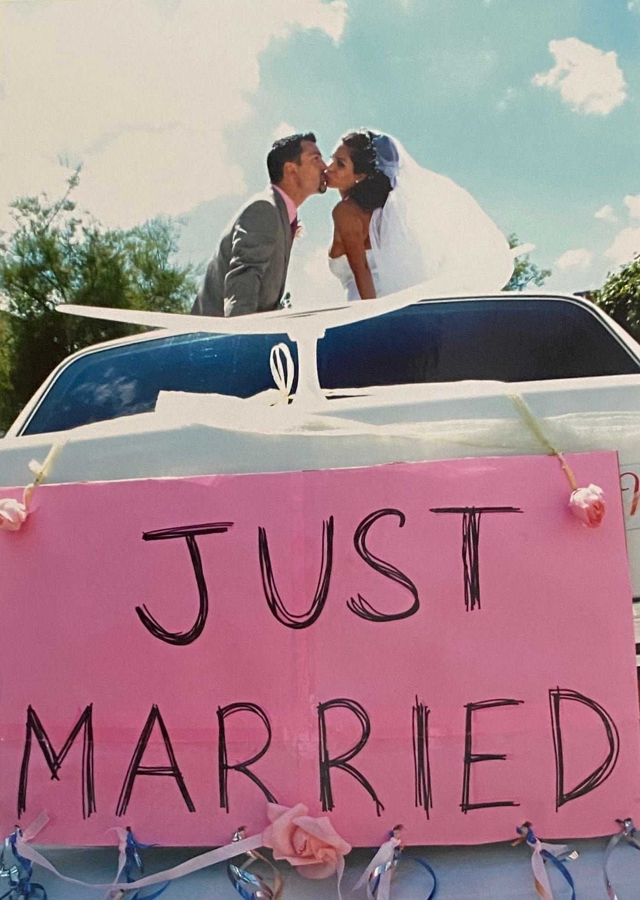 Ein Brautpaar küsst sich auf einer Limousine mit "Just Married"-Schild und rosa Dekoration.