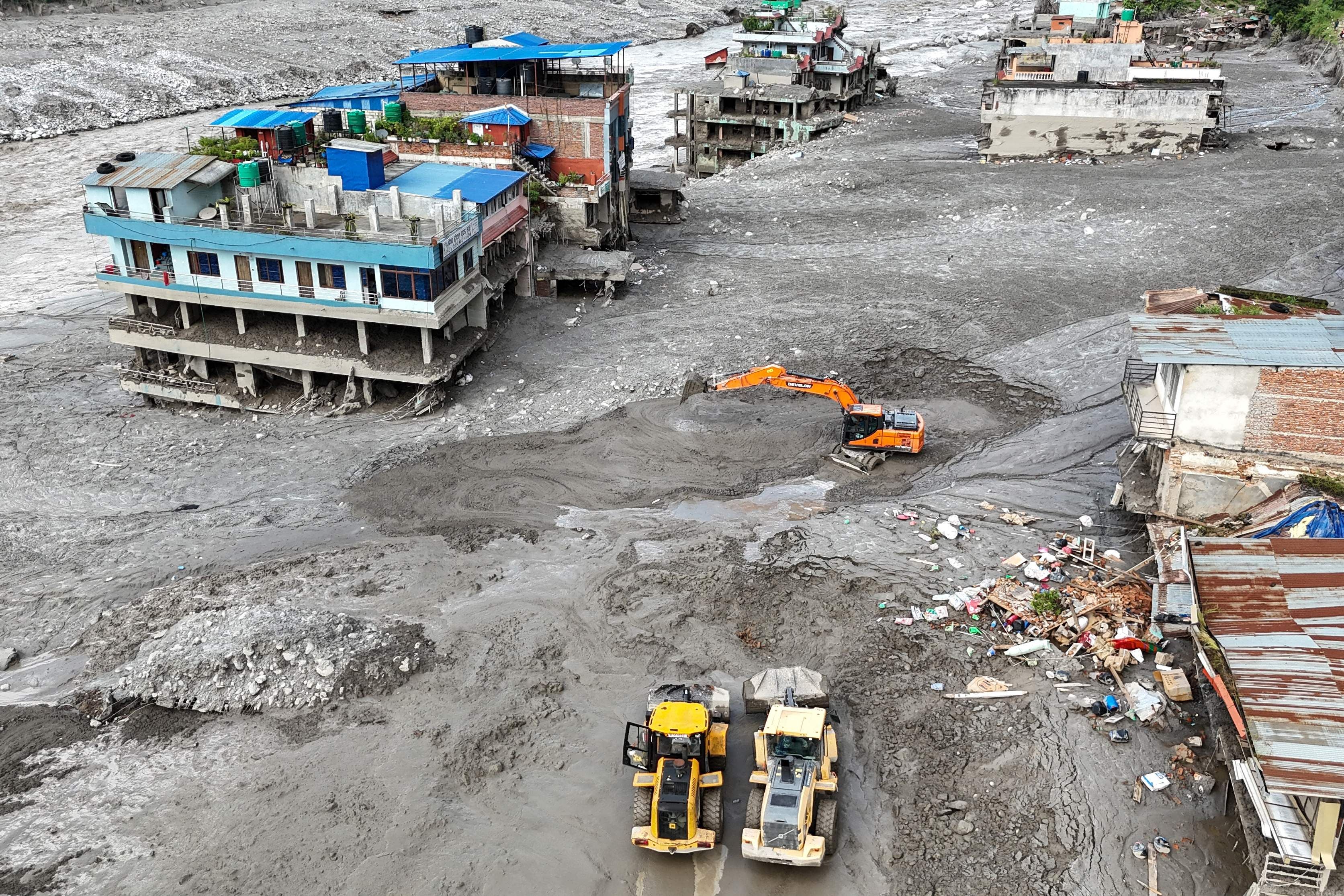Bagger räumen Schlammmassen zwischen beschädigten Häusern nach Überschwemmung in Nepal.