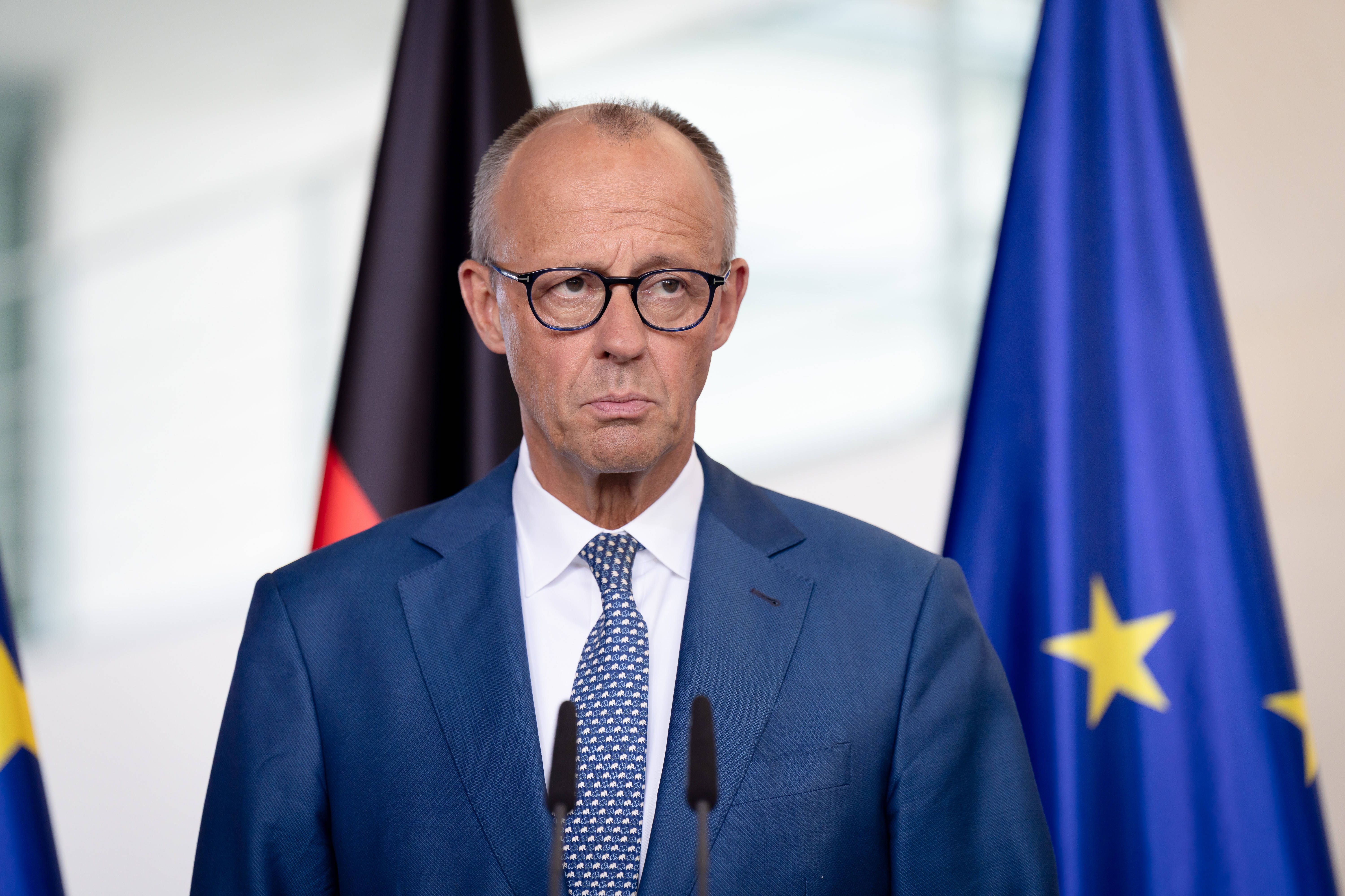 Ein Mann im blauen Anzug steht vor deutschen und EU-Flaggen bei einer Pressekonferenz.