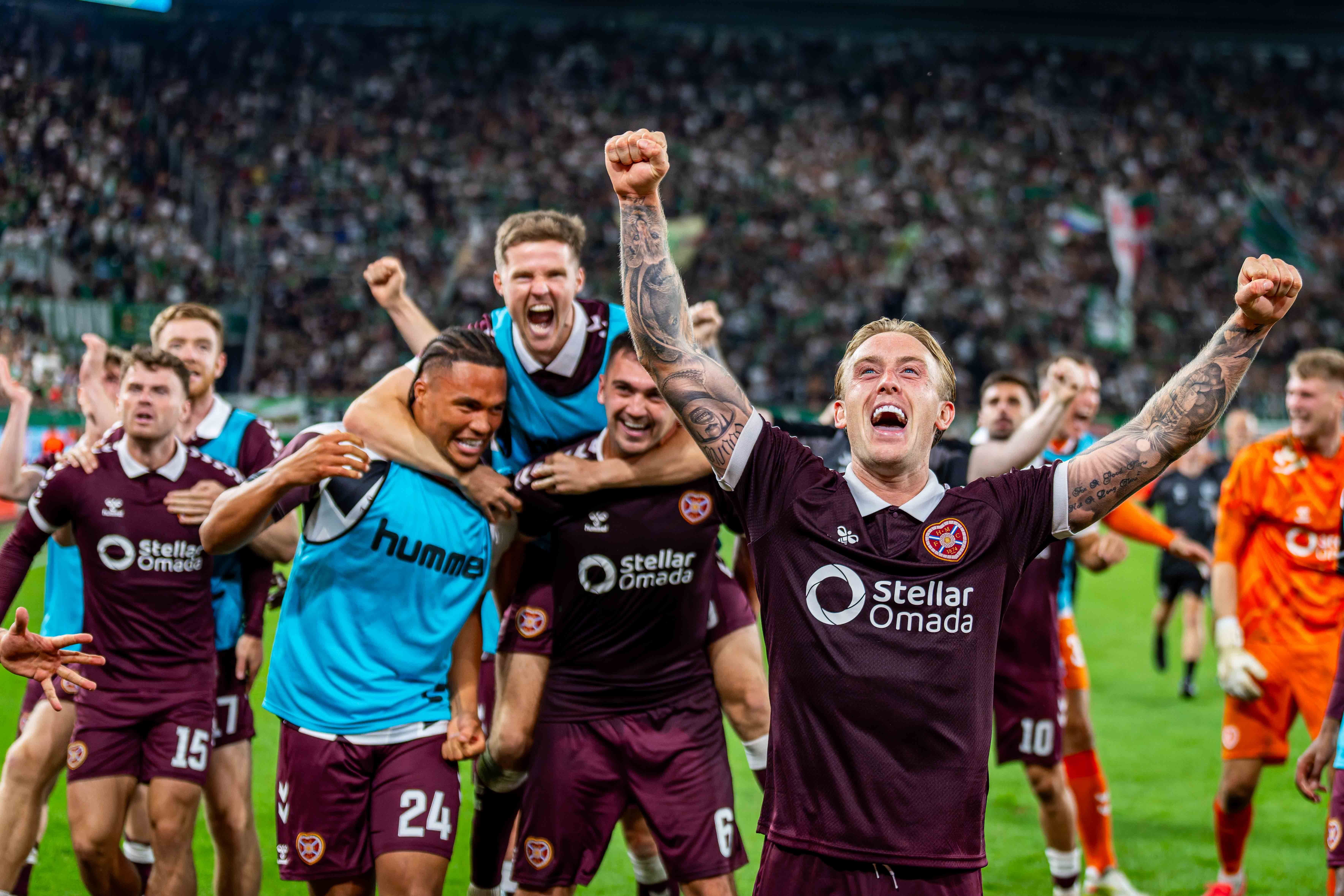 Jubelnde Hearts-Spieler feiern auf dem Fußballfeld nach einem Sieg gegen Rapid Wien.