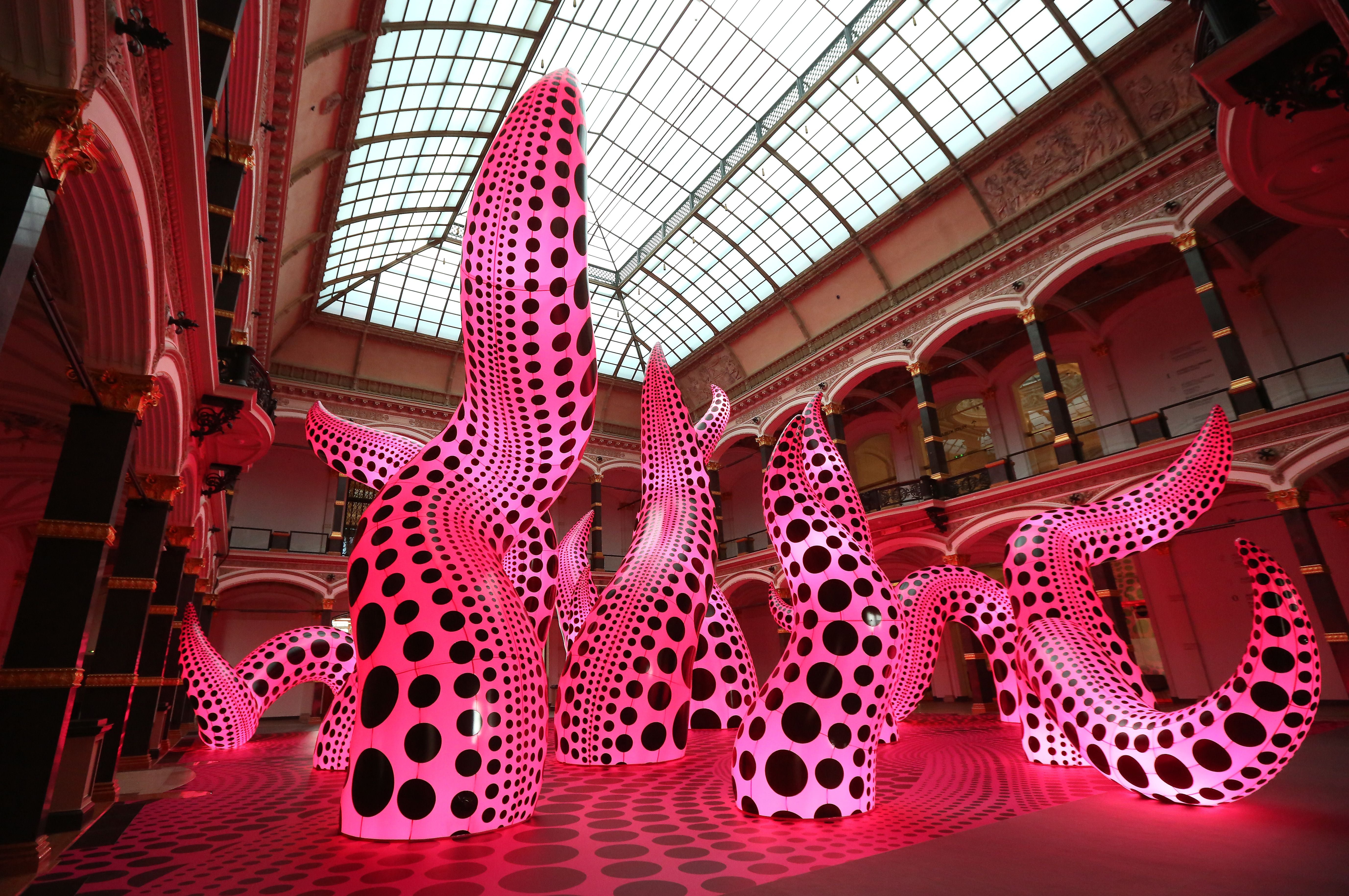 Große, pink leuchtende Skulpturen mit schwarzen Punkten in einer Ausstellungshalle.