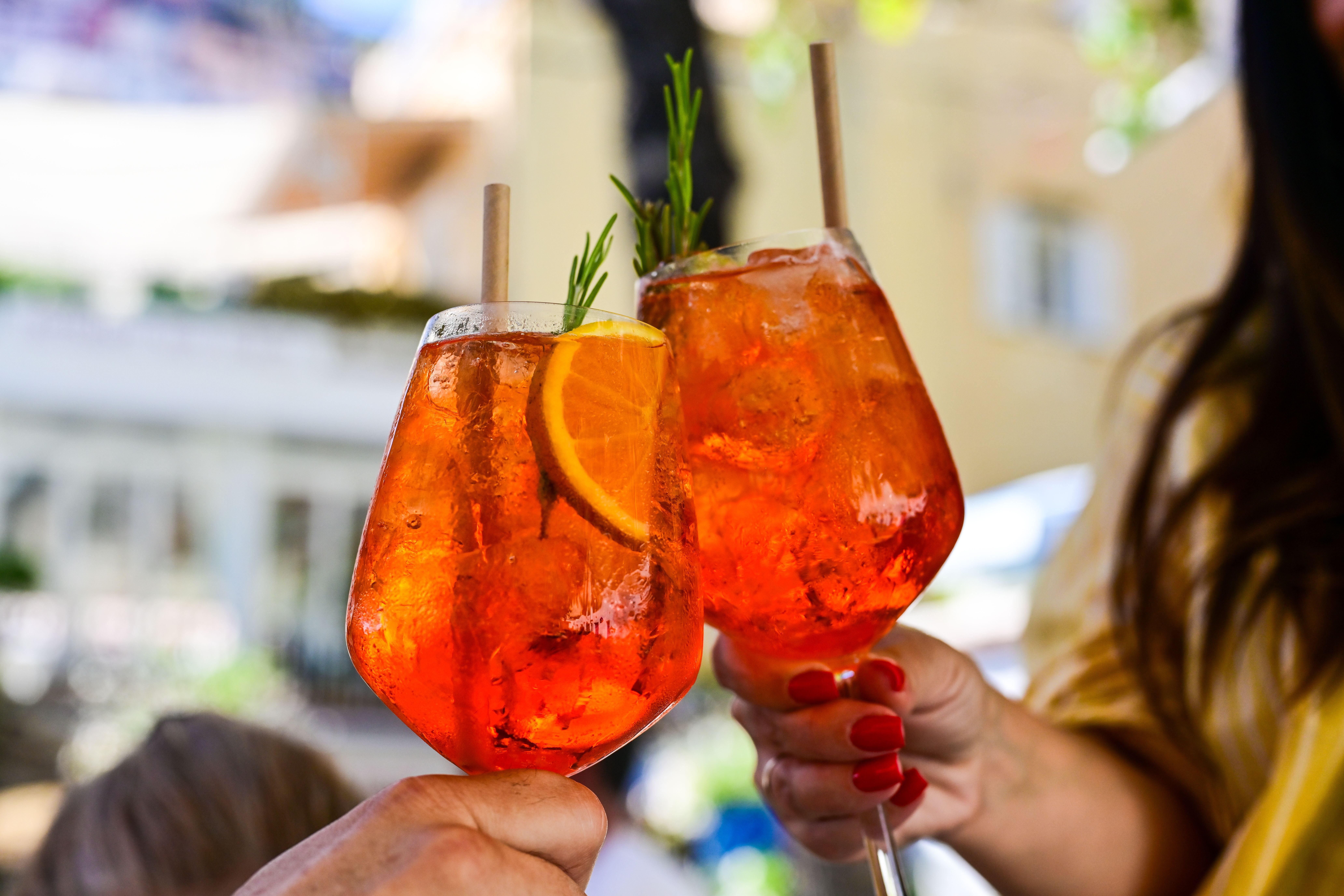 Zwei Hände stoßen mit Spritz-Cocktails mit Orangenscheibe und Kräutergarnitur an.