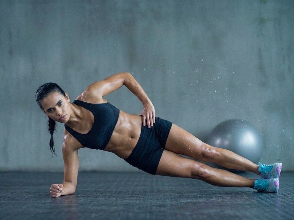 Sportliche Frau macht einen seitlichen Plank auf einer Trainingsmatte in einem Fitnessstudio.