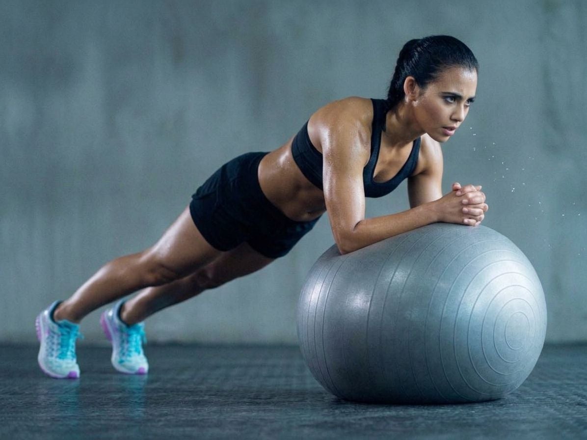 Frau macht Plank-Übung auf einem Gymnastikball in Sportkleidung und Sportschuhen.
