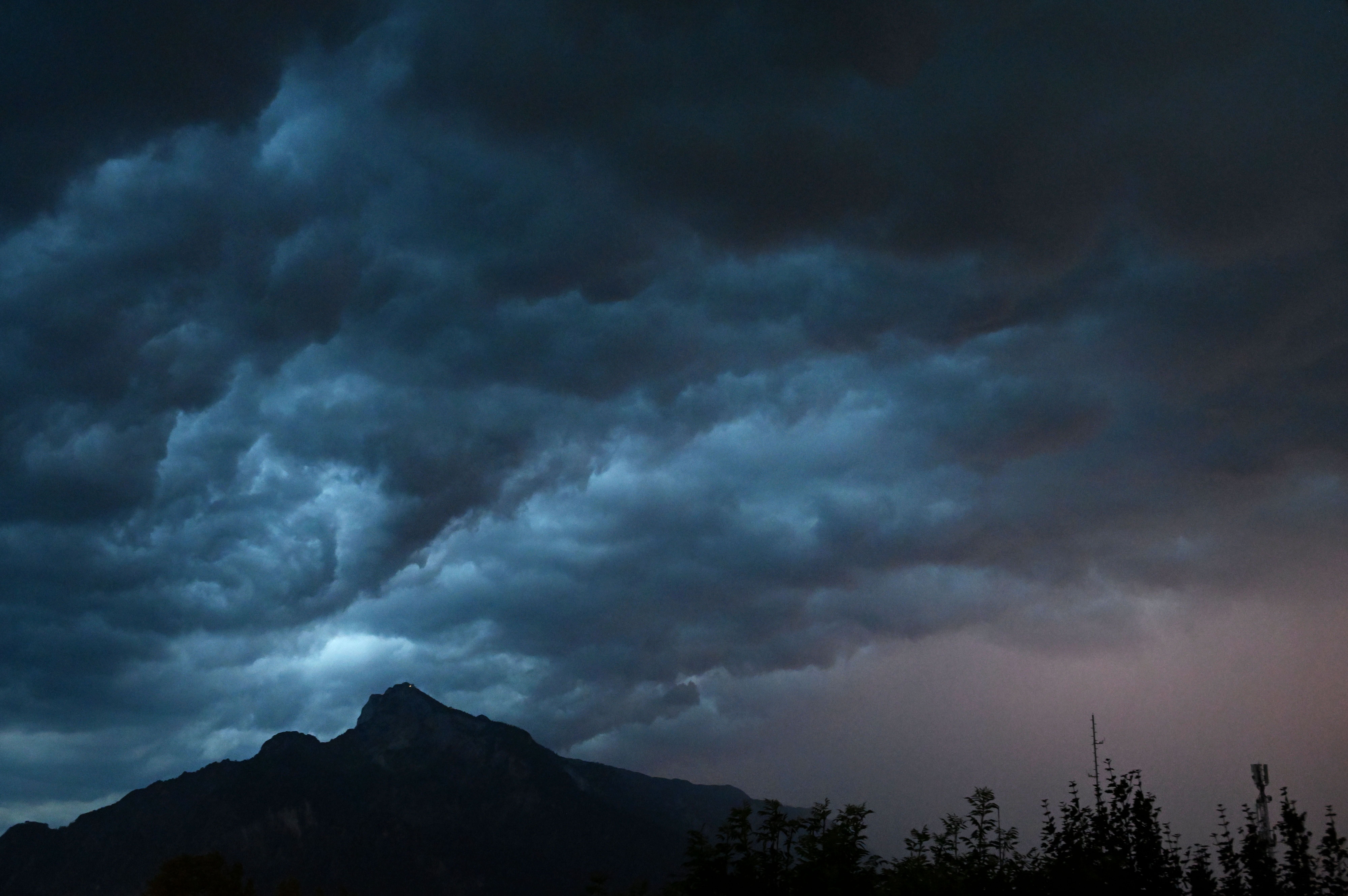 Dunkle Gewitterwolken leuchten über dem Untersberg bei Salzburg in der Dämmerung.