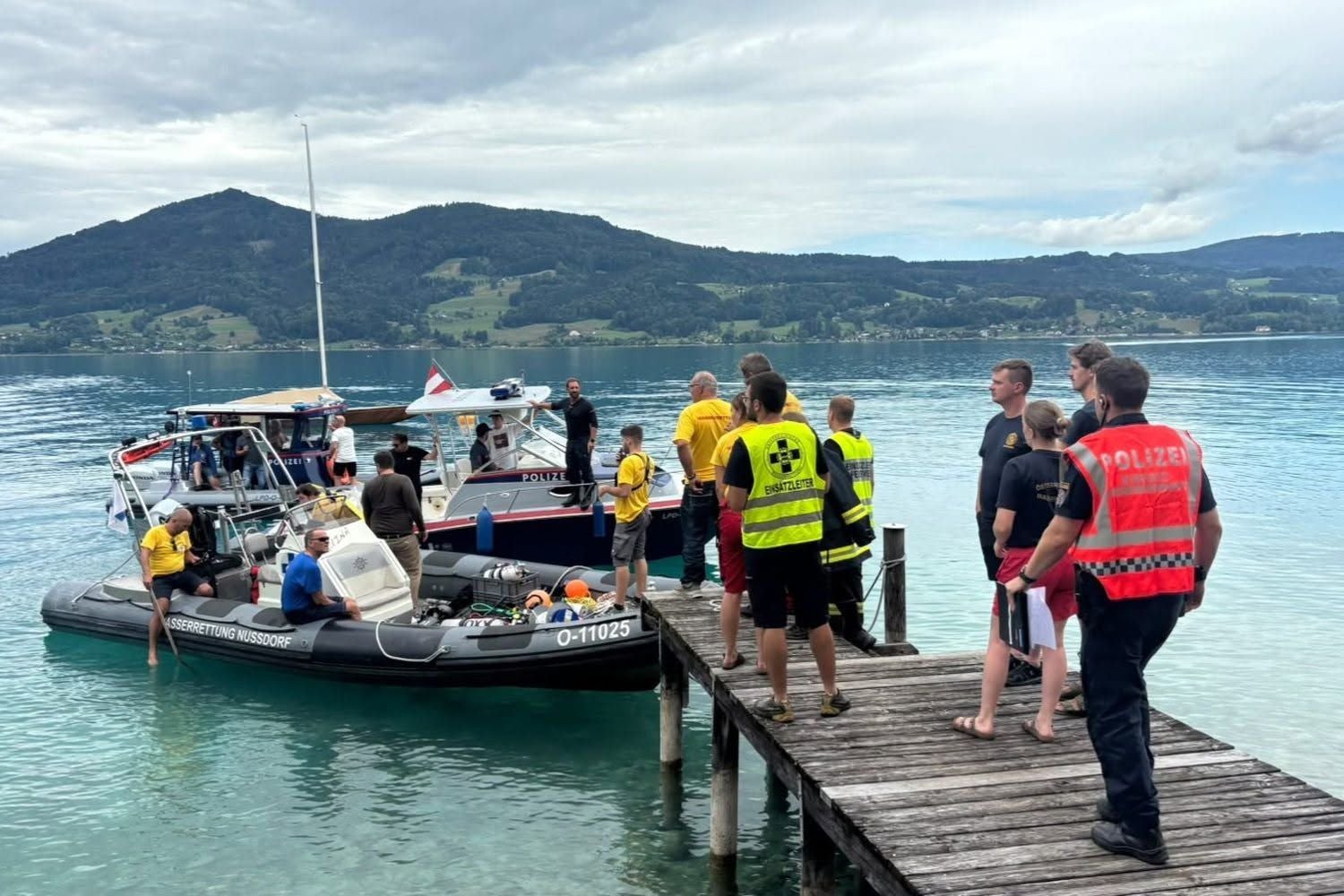 Einsatzkräfte und Polizei stehen an einem Steg mit Rettungsbooten am Attersee.