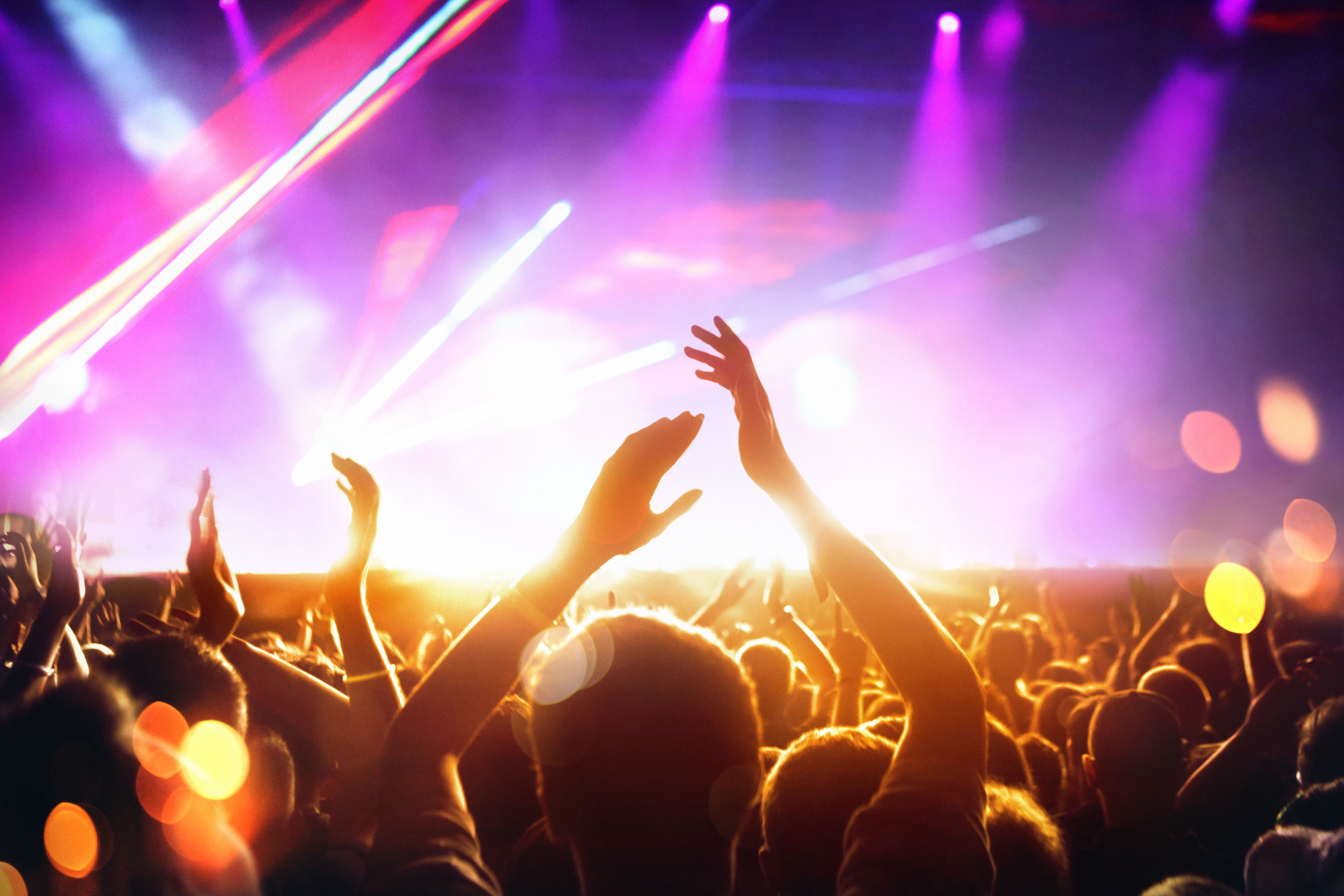 Menschenmenge feiert bei einem Konzert mit bunten Lichtern und erhobenen Armen.