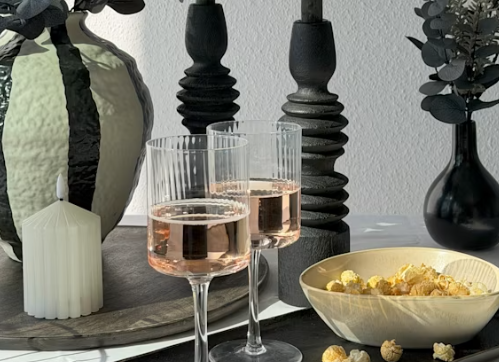Zwei Weingläser mit Roséwein stehen neben einer Schale Popcorn und Dekoration auf einem Tisch.