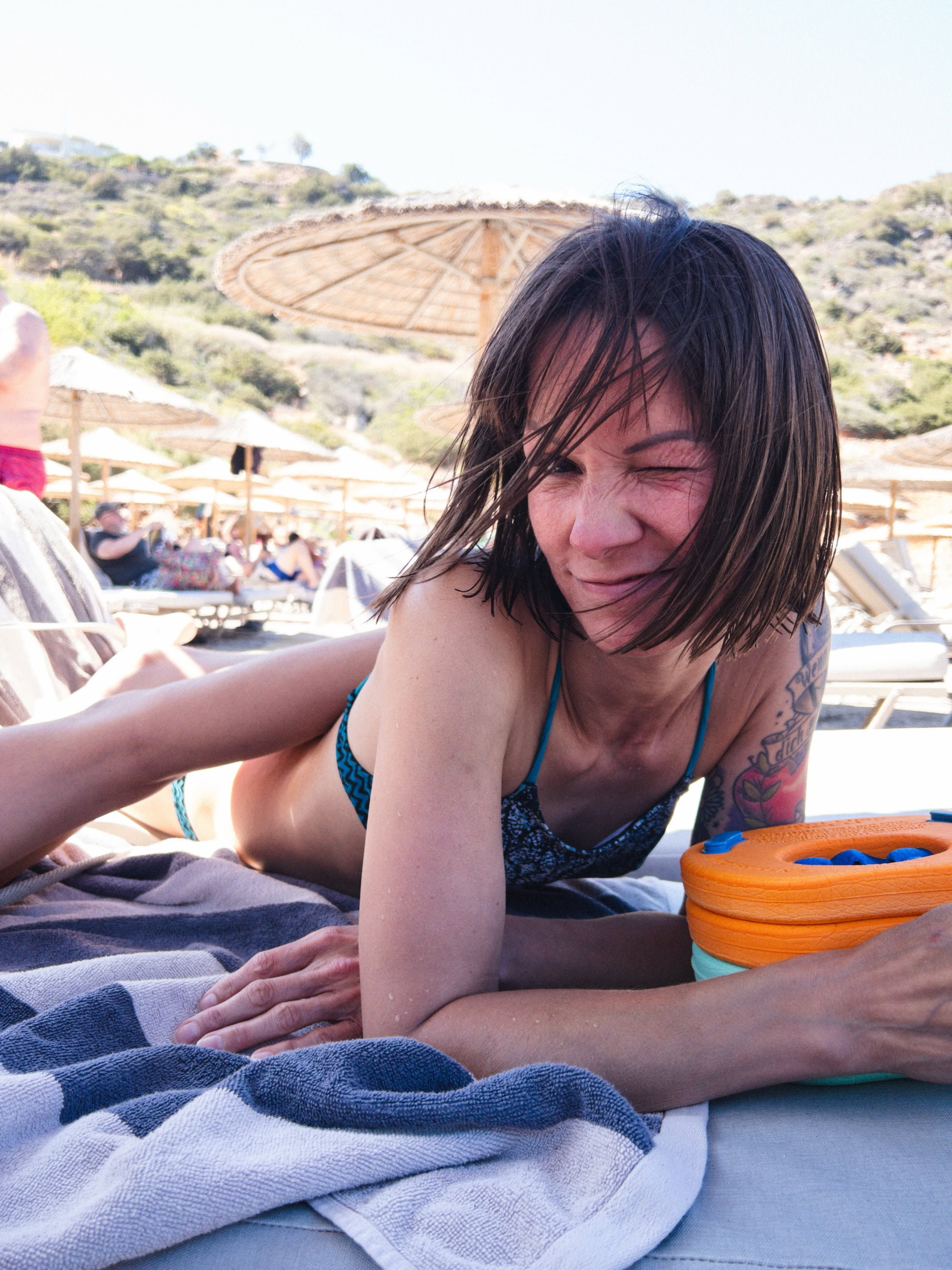 Eine Frau im Bikini liegt auf einem Strandhandtuch und zwinkert in die Kamera.