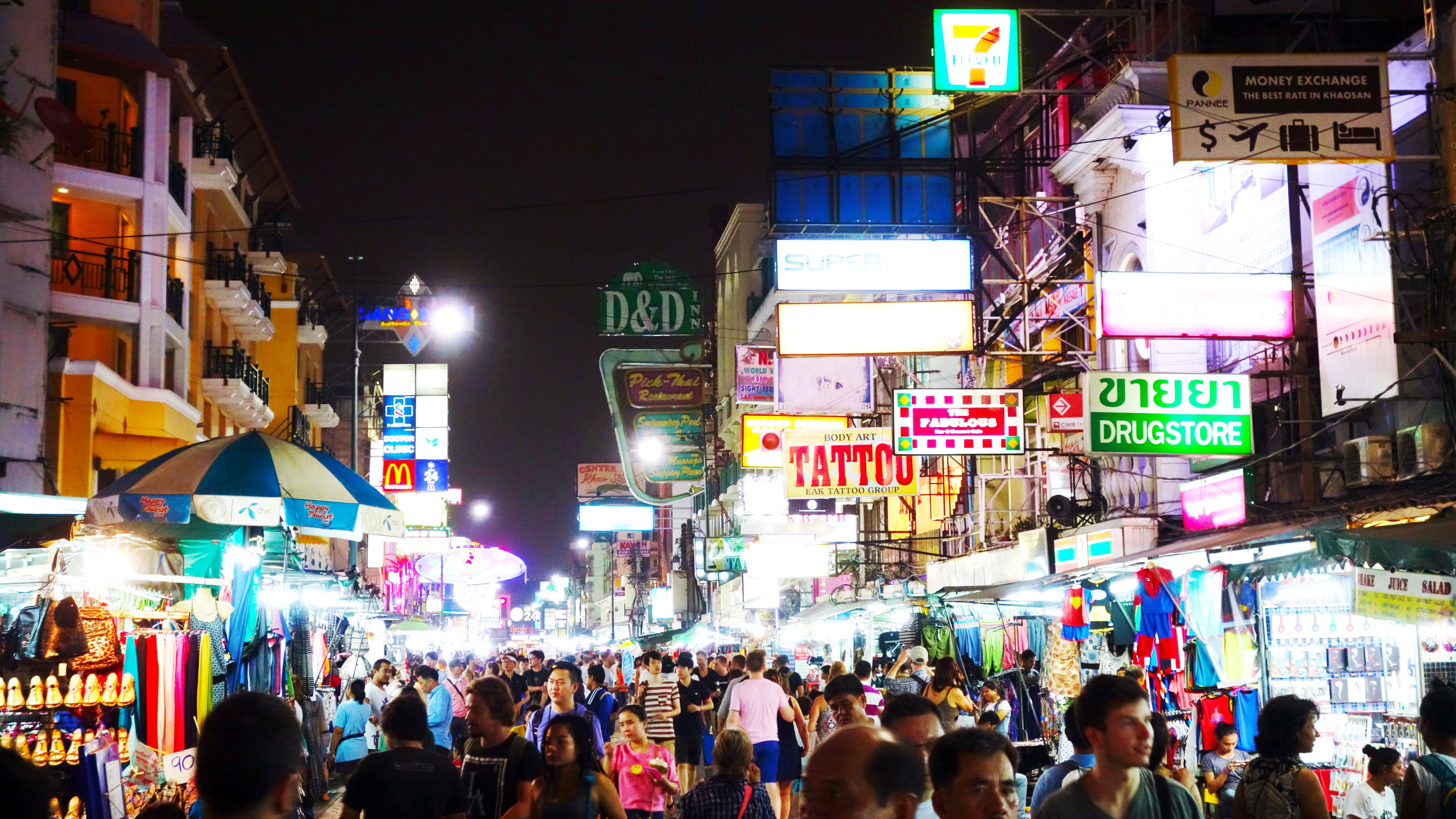 Belebte Khao San Road in Bangkok bei Nacht mit vielen Menschen und bunten Leuchtreklamen.
