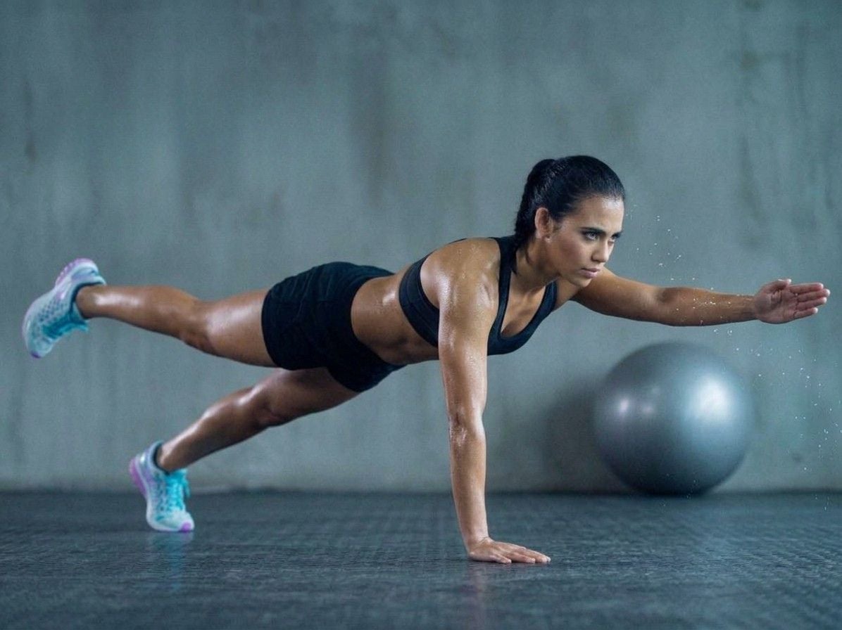 Frau macht anstrengende Fitnessübung im Plank mit ausgestrecktem Arm und Bein.