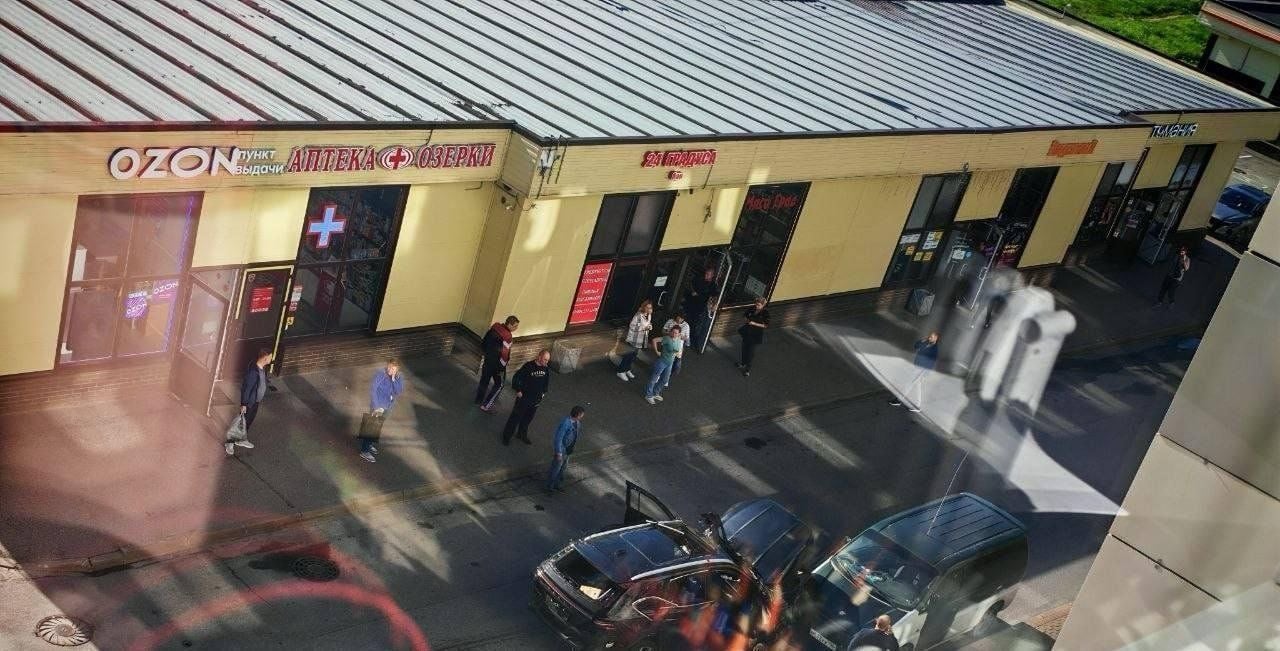 Menschen stehen vor einem Einkaufszentrum in Sankt Petersburg, zwei Autos parken davor.