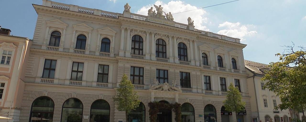 Historisches Gebäude der Sparkasse OÖ mit Statuen auf dem Dach und Bäumen davor.