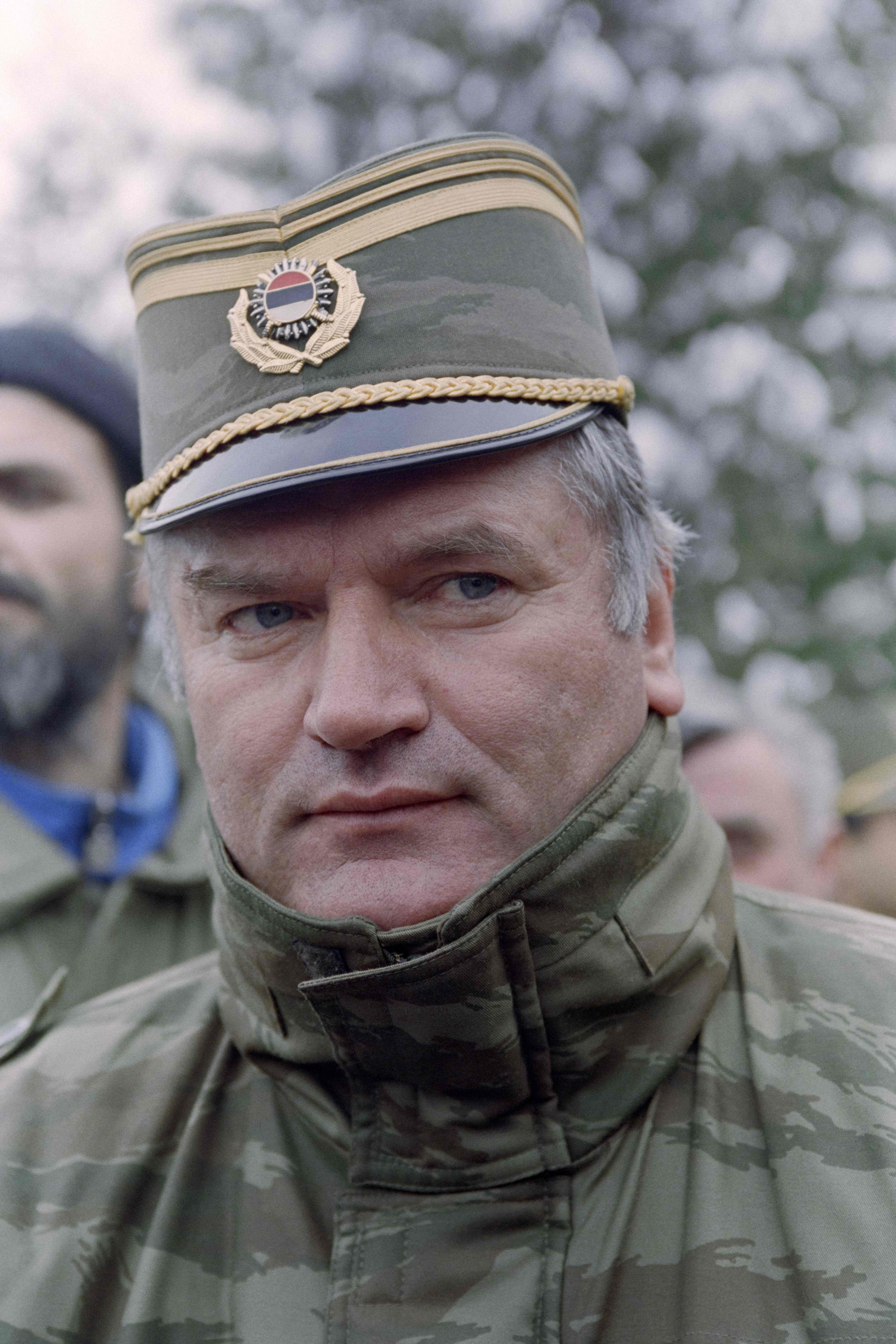 Ein Mann in Militäruniform und Mütze blickt ernst in die Kamera, im Freien aufgenommen.
