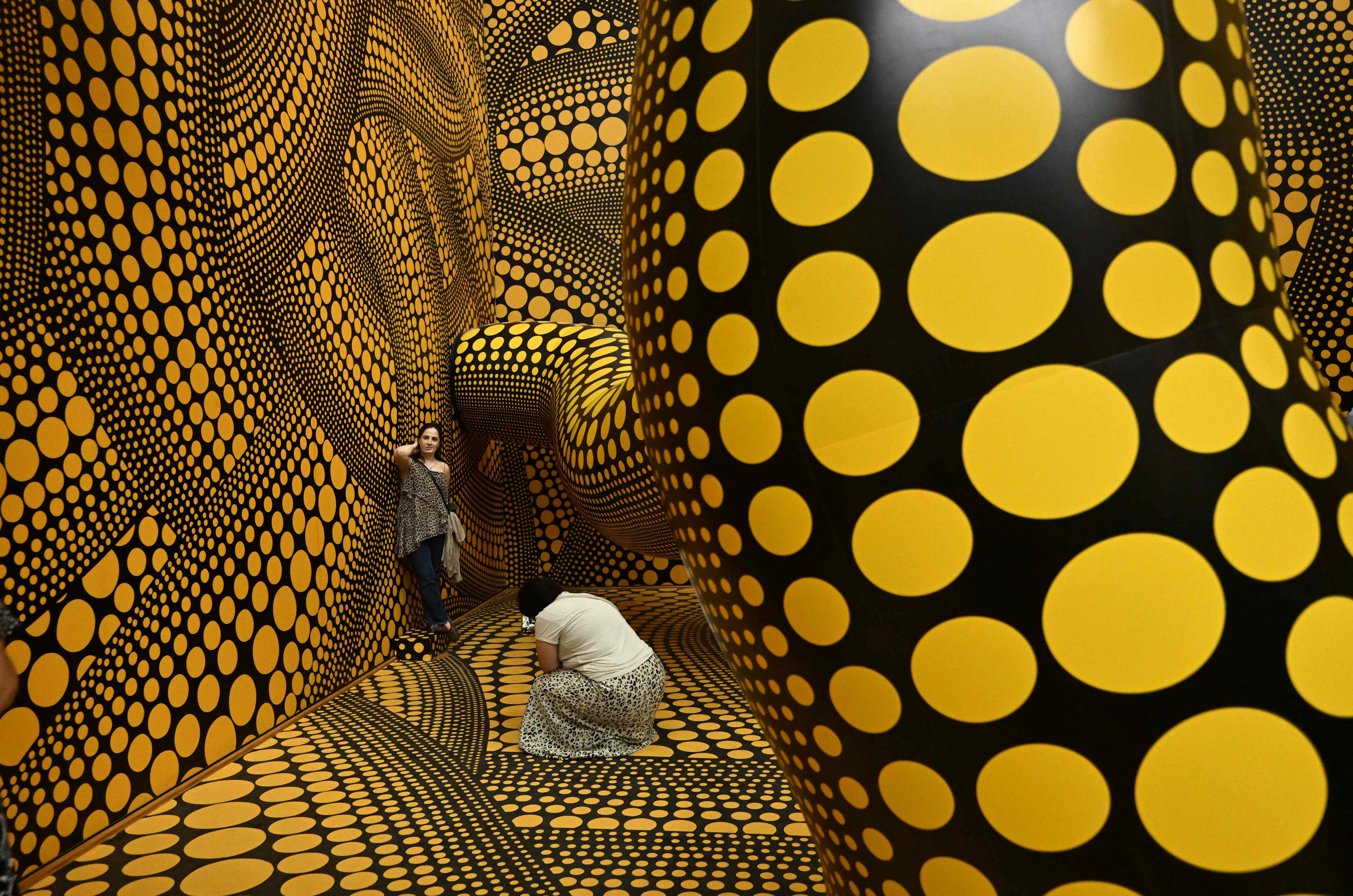 Zwei Besucher fotografieren sich in einem Raum mit gelb-schwarzem Polka-Dot-Muster von Kusama.