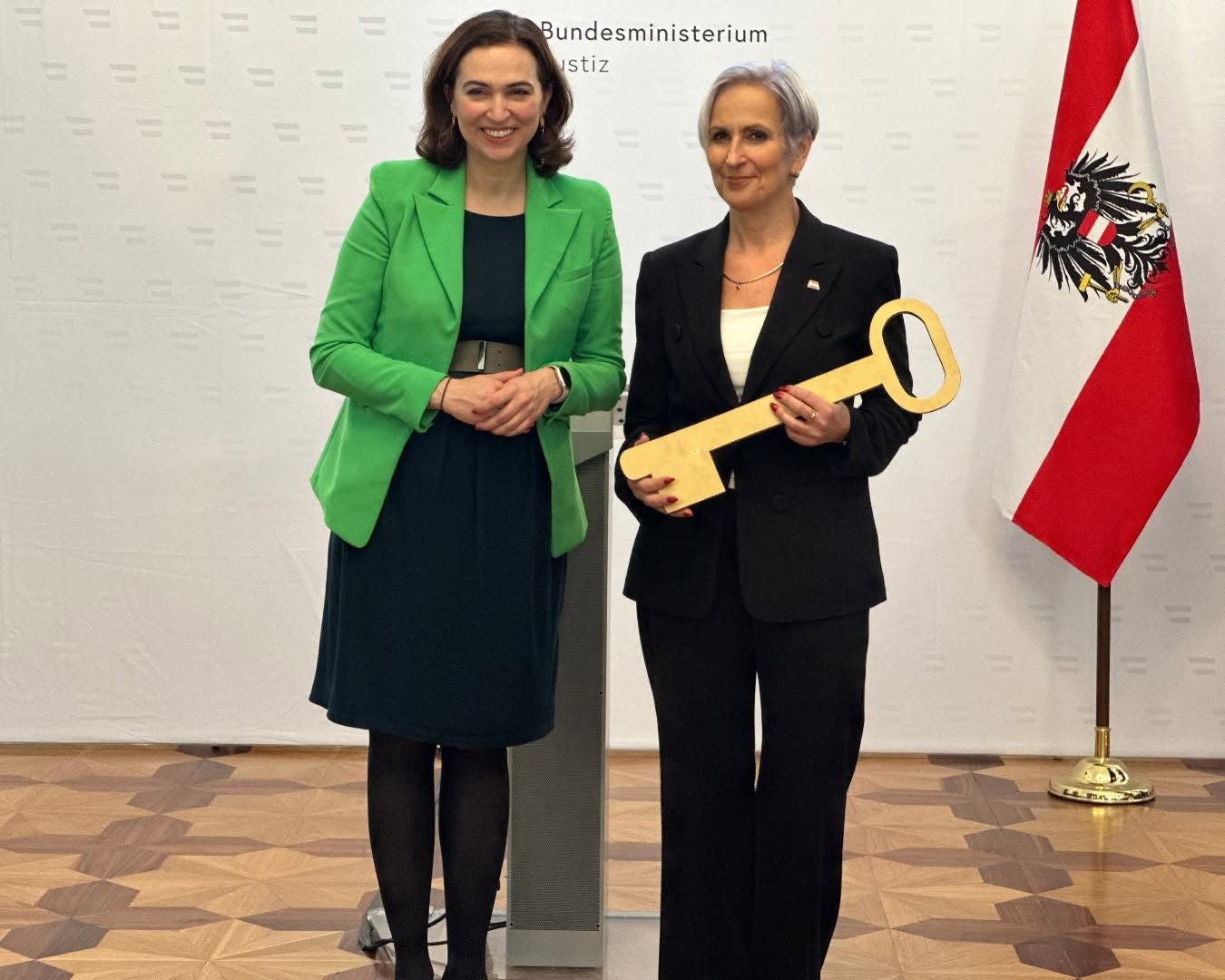 Zwei Frauen stehen nebeneinander, eine hält einen großen symbolischen Schlüssel.