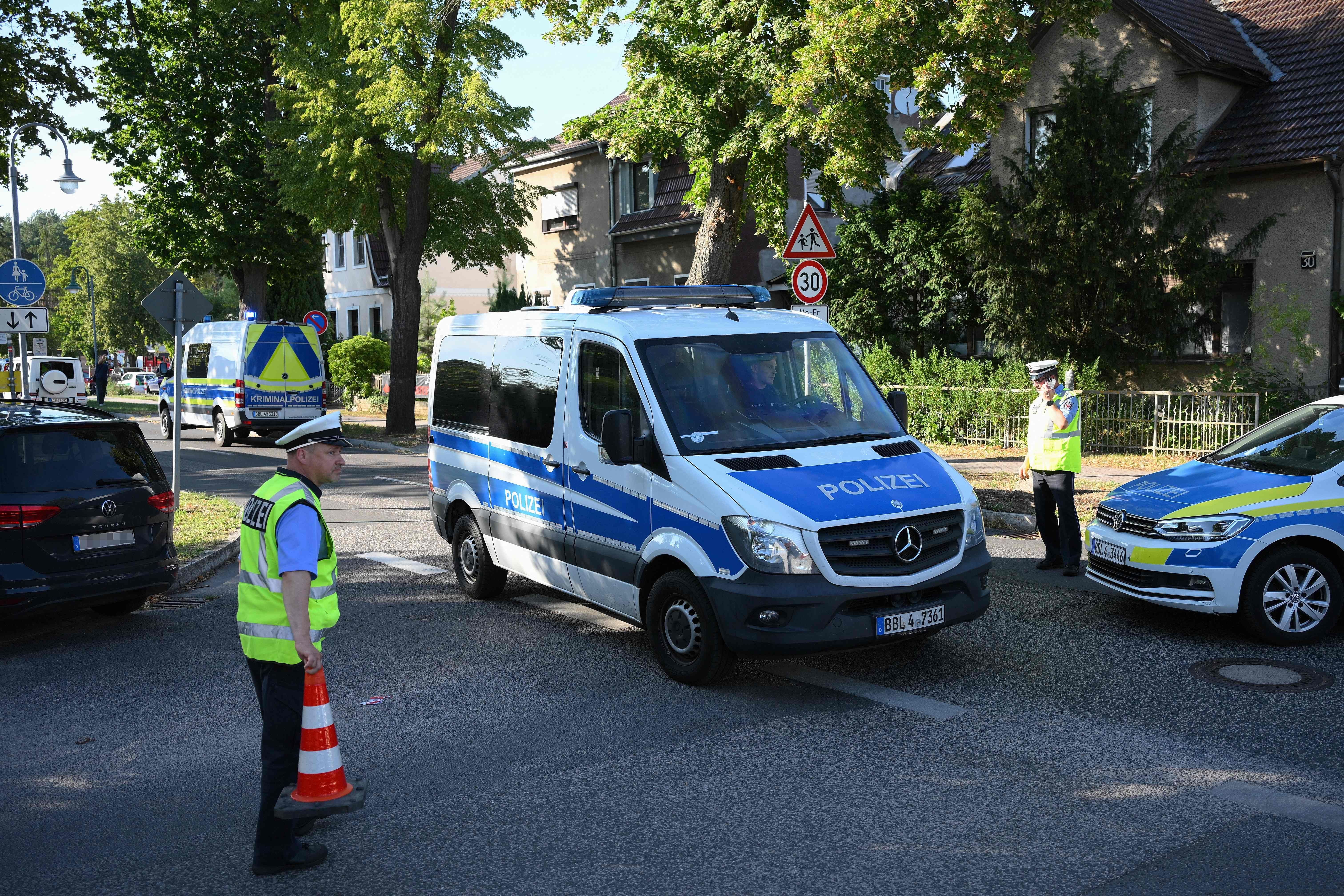 Polizisten und mehrere Polizeifahrzeuge sperren eine Straße in einem Wohngebiet ab.