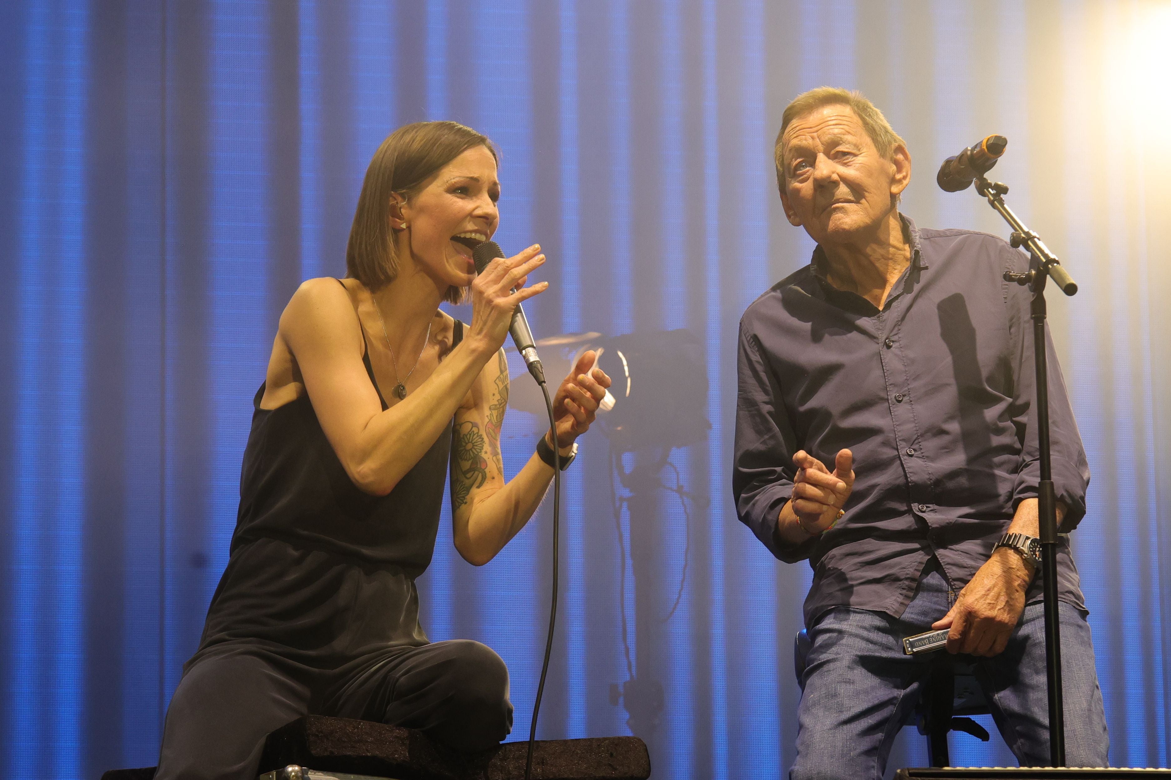 Eine Frau und ein älterer Mann singen gemeinsam auf einer Bühne mit blauem Licht.