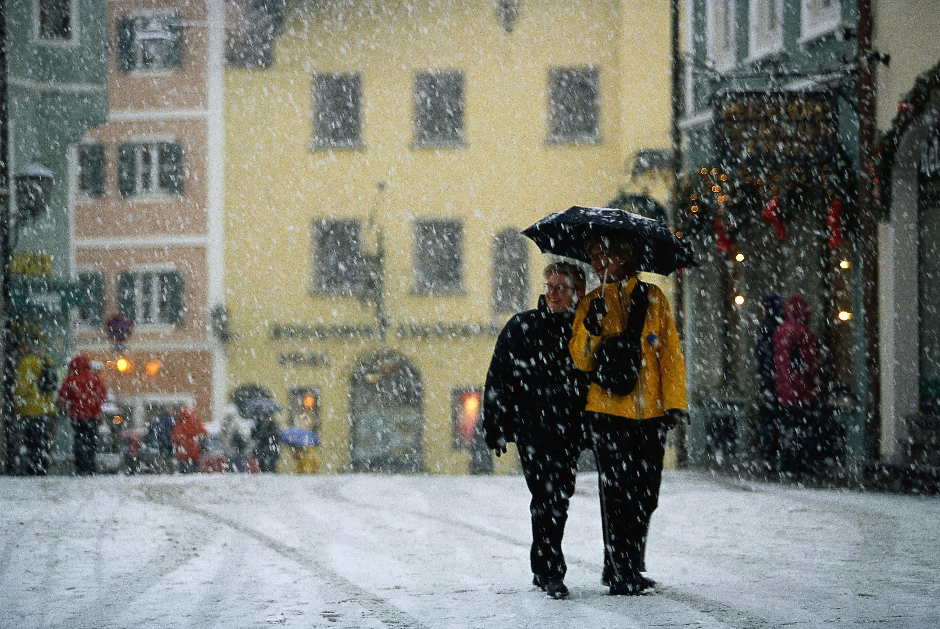 Zwei Personen gehen bei starkem Schneefall mit einem Regenschirm durch eine verschneite Stadt.
