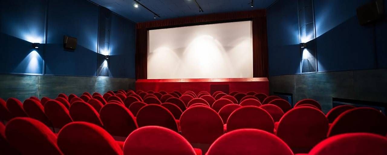 Kinosaal mit roten Sitzen und leerer Leinwand, Wände blau beleuchtet.