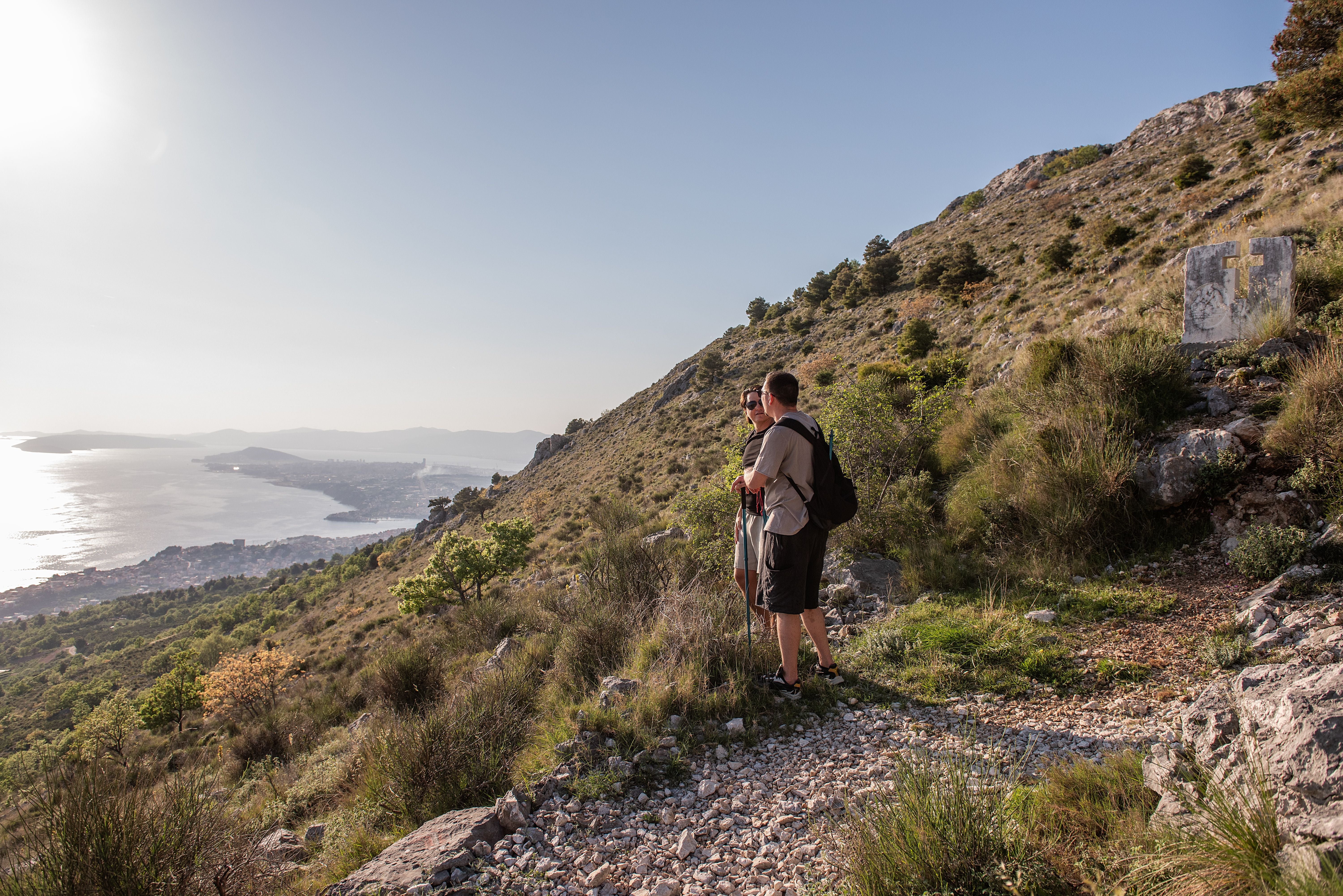 Zwei Wanderer stehen auf einem felsigen Pfad mit Blick auf die Adriaküste und Split in Kroatien.