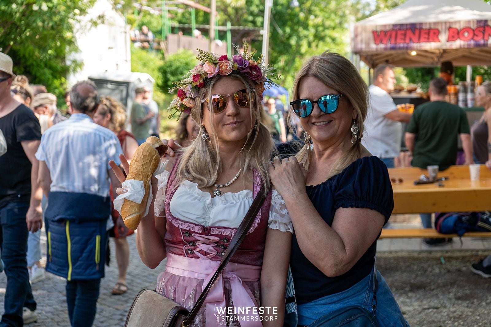 Zwei Frauen mit Sonnenbrillen beim Stammersdorfer Weinfest, eine trägt Dirndl und Blumenkranz.