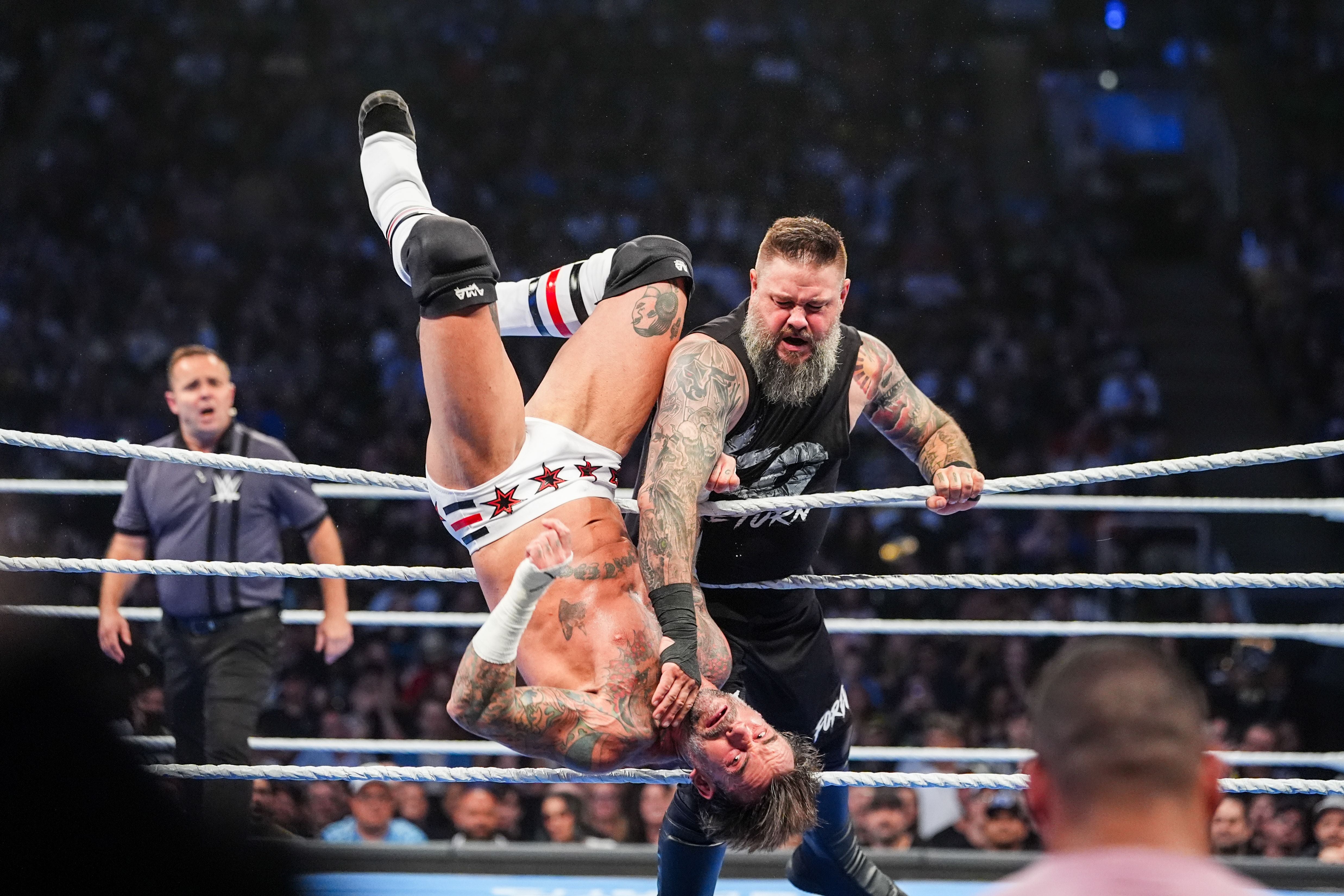 Zwei Wrestler kämpfen im Ring vor großem Publikum, einer hebt den anderen kopfüber hoch.