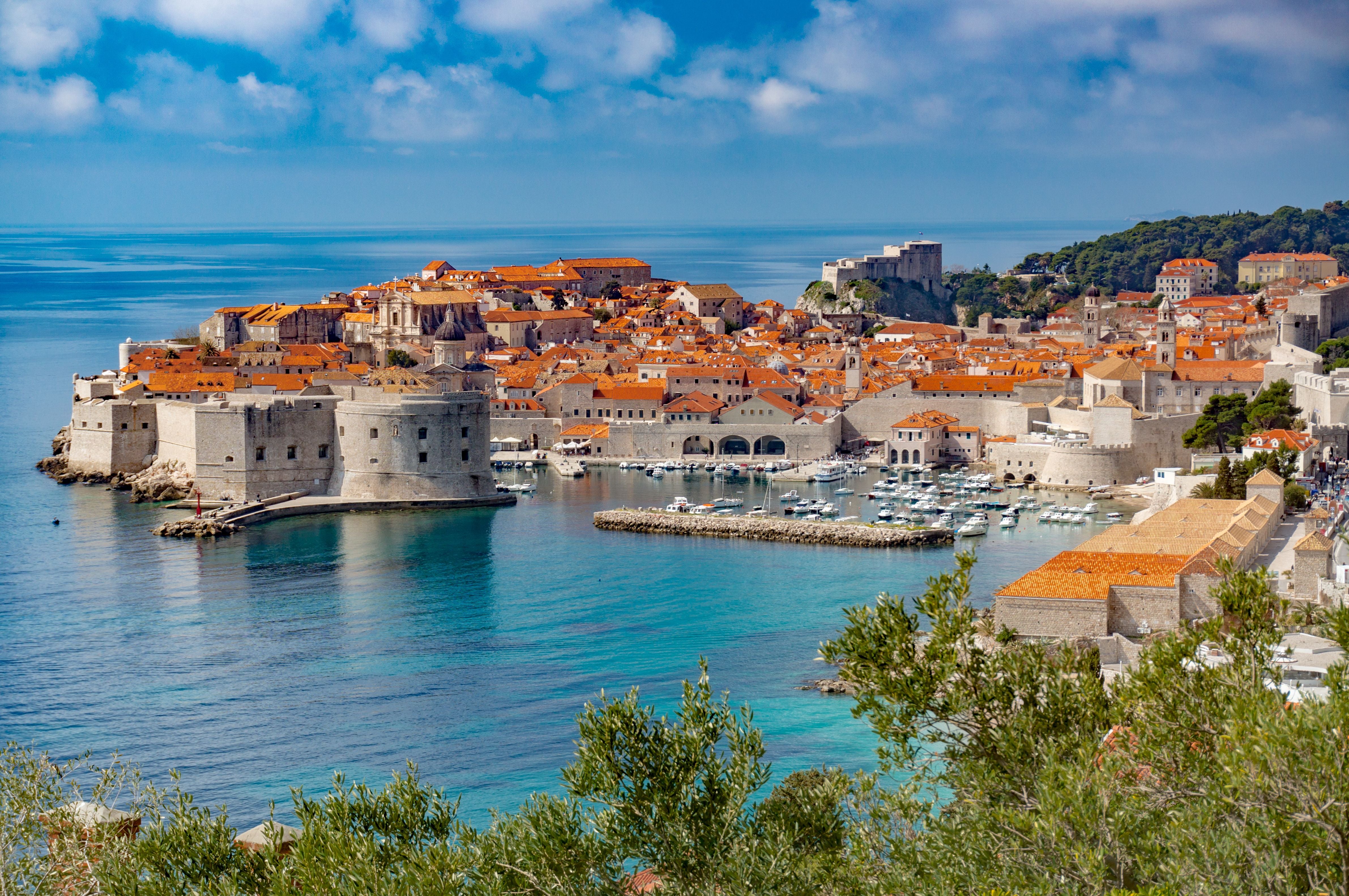 Panorama der Altstadt von Dubrovnik mit roten Dächern und Hafen am blauen Meer.
