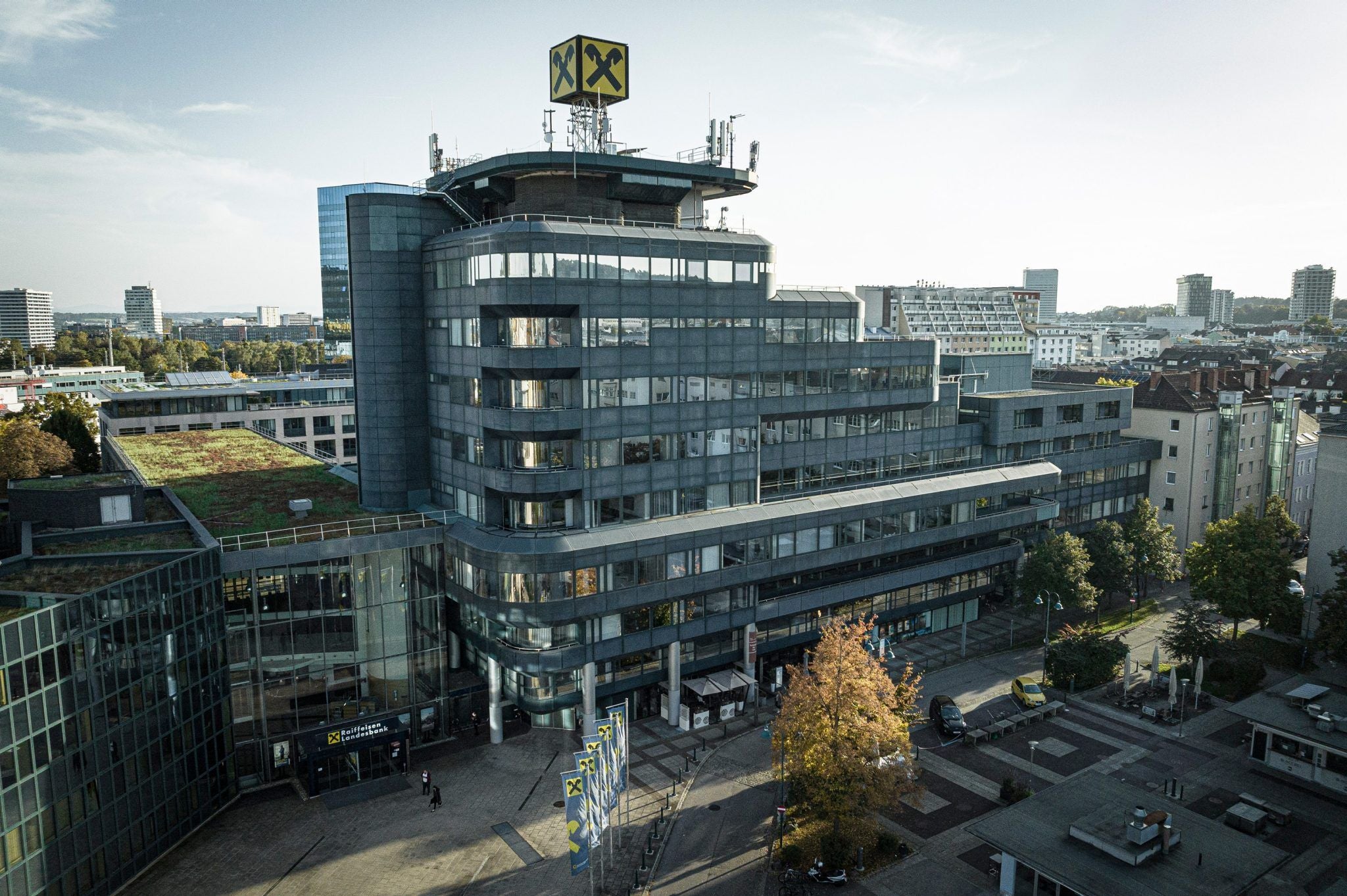 Modernes Bürogebäude der Raiffeisenbank mit markantem gelbem Logo auf dem Dach in einer Stadtumgebung.