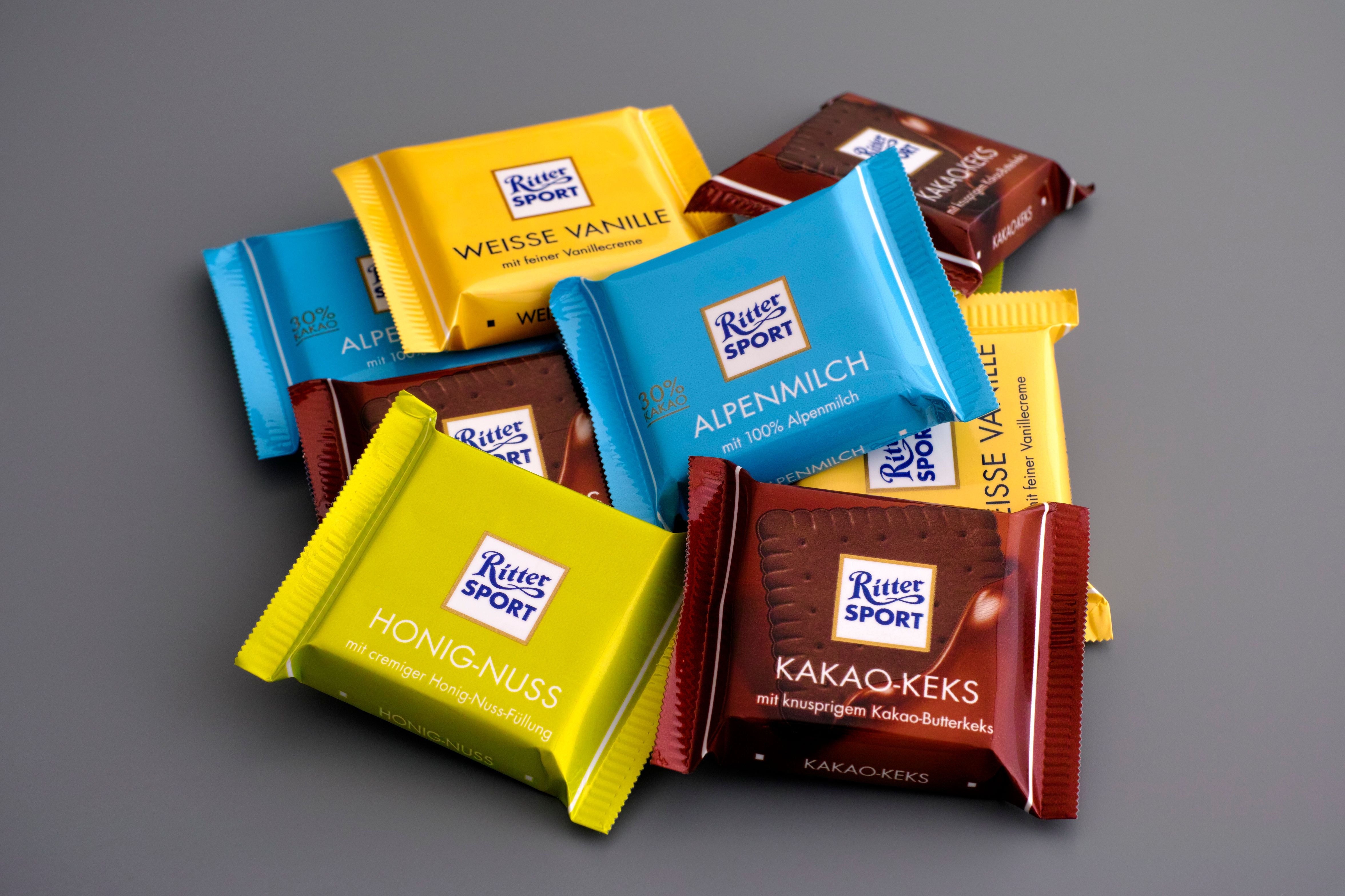 Verschiedene Ritter Sport Mini-Schokoladen liegen auf grauem Hintergrund.