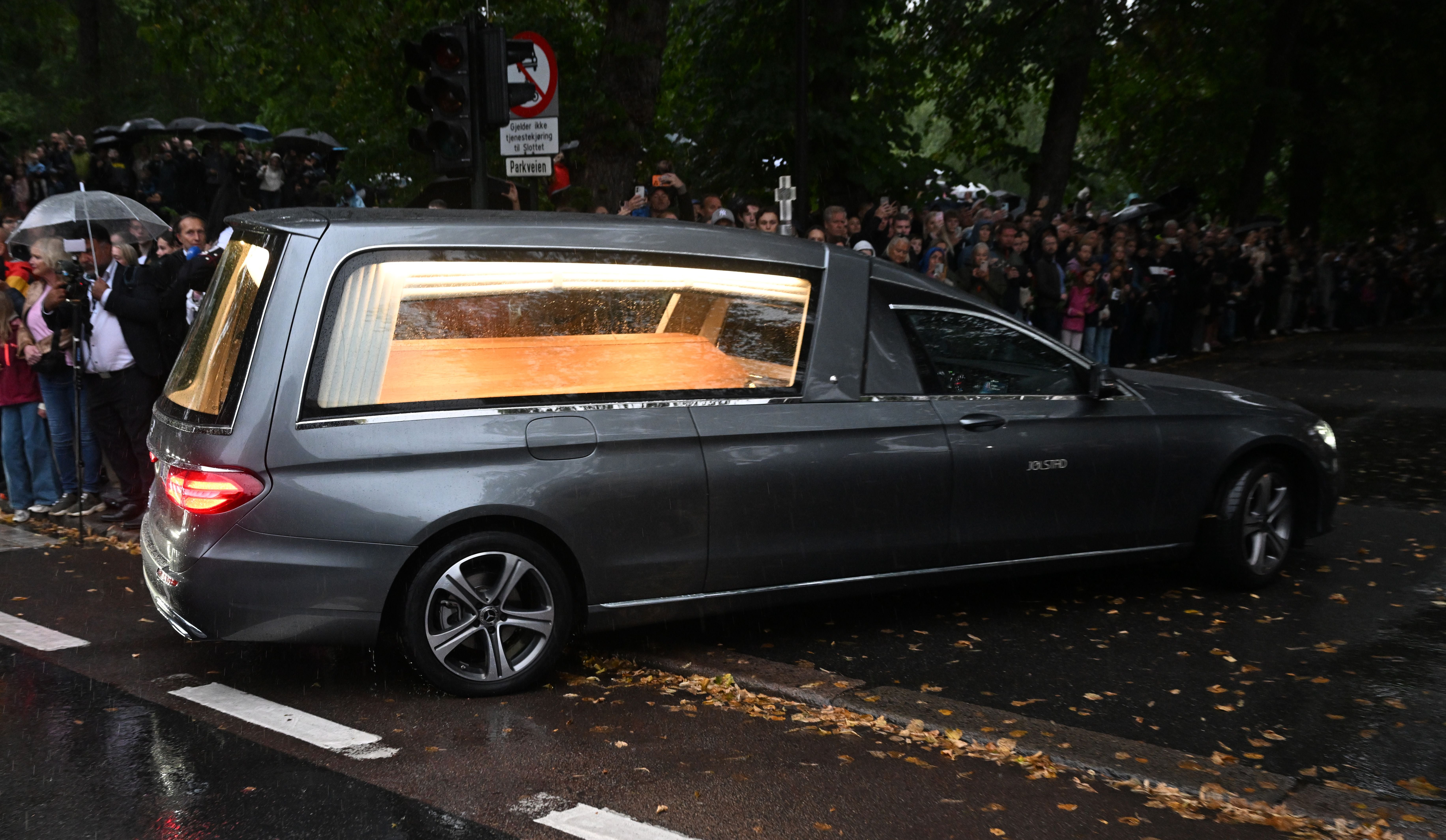 Ein Leichenwagen mit einem Sarg fährt bei Regen an einer wartenden Menschenmenge in Oslo vorbei.