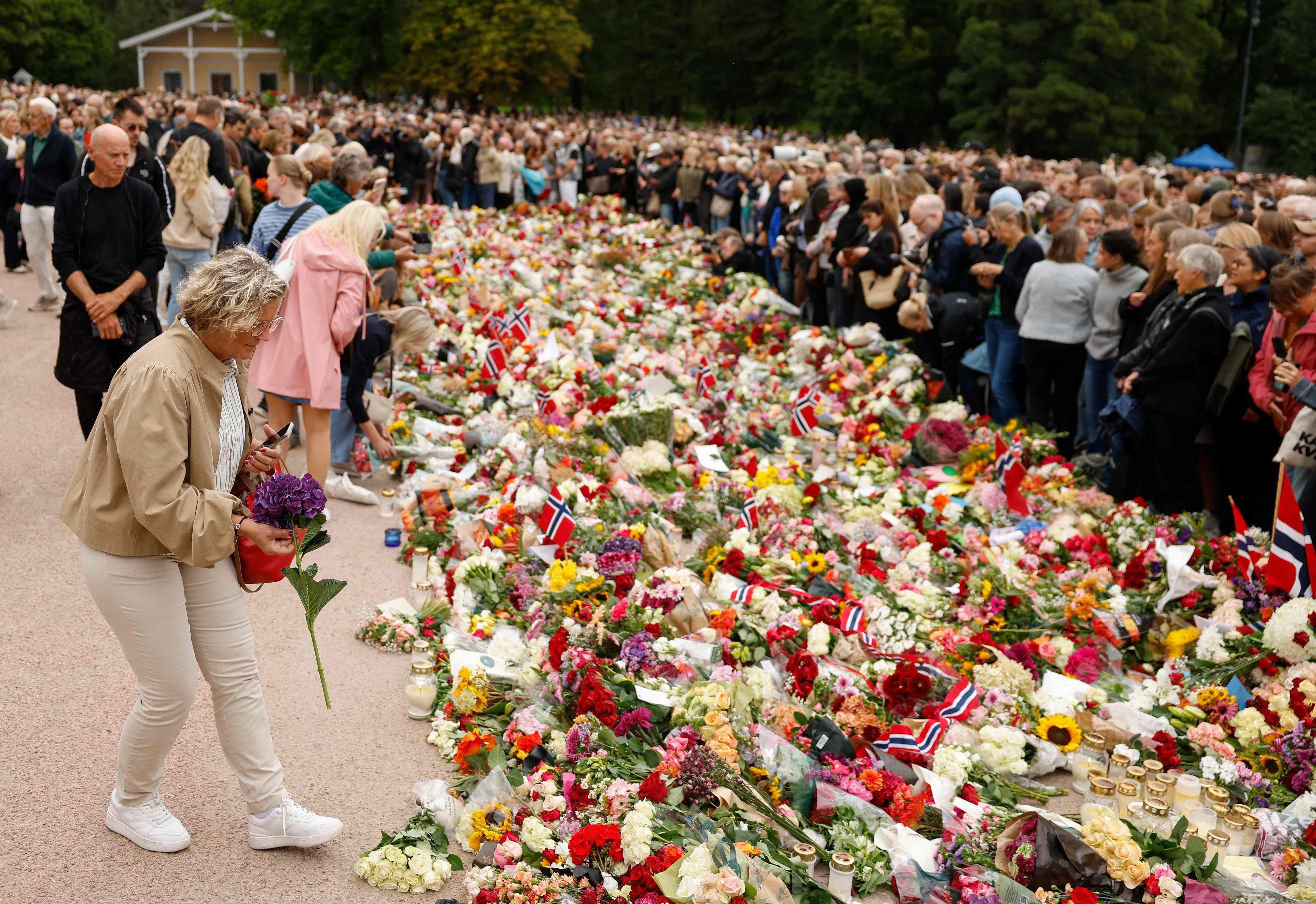 Viele Menschen legen Blumen an einem Gedenkort mit norwegischen Flaggen nieder.